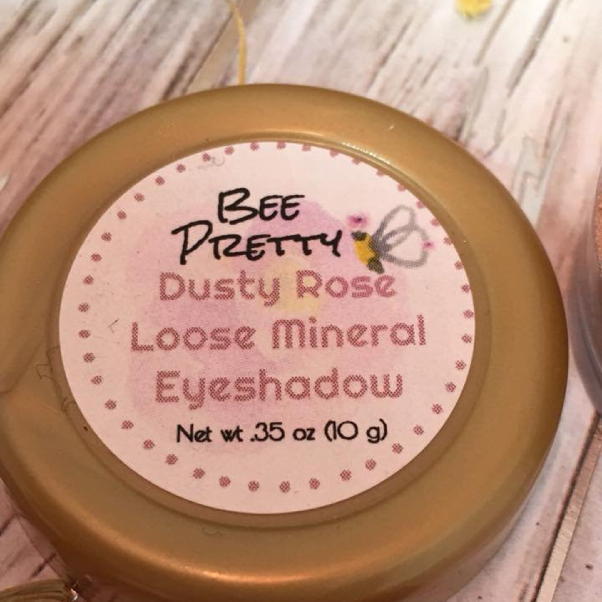 Close-up of loose mineral eyeshadow in soft dusty rose shade with fine shimmer particles inside clear jar