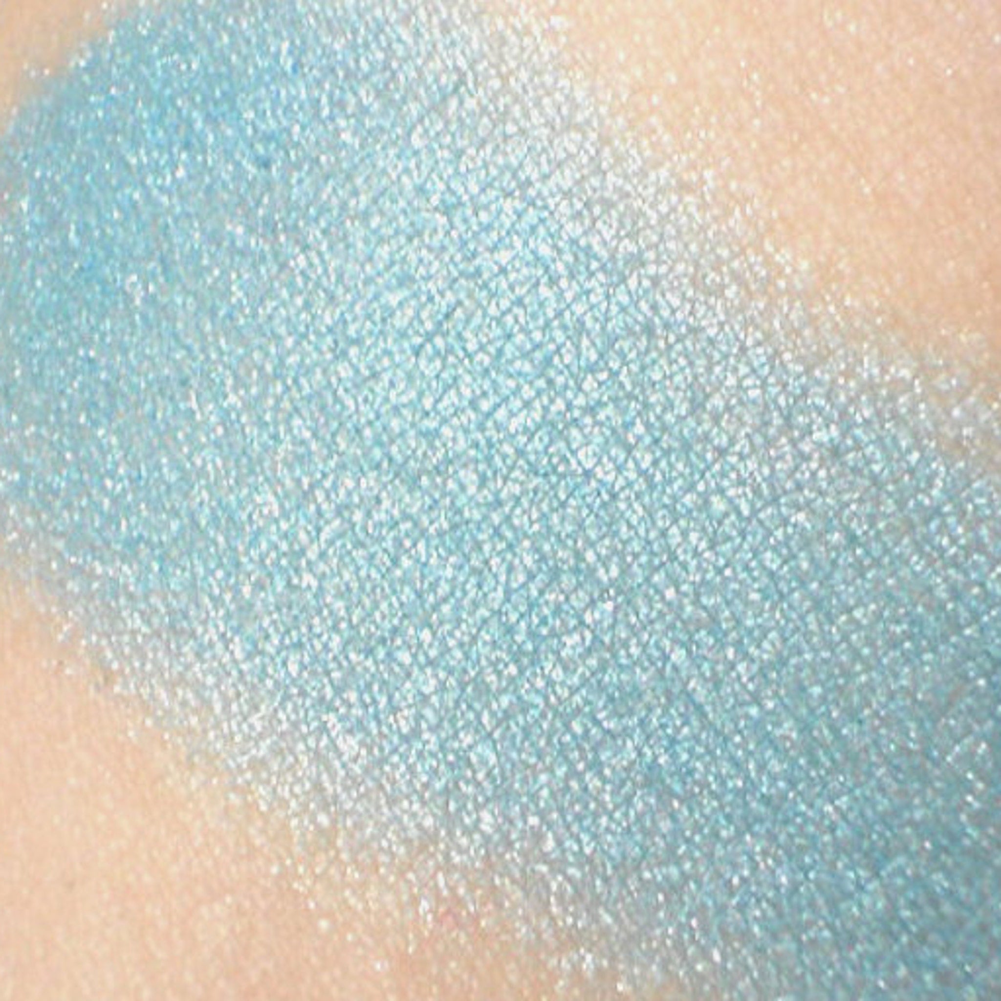 Side-angle view of frosty aqua blue mineral eyeshadow with shimmer in compact, showcasing reflective texture