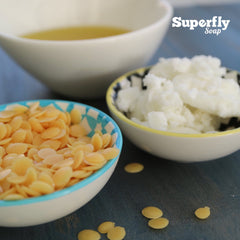 Beeswax pellets and oil in bowls with Superfly Soap logo on a blue surface