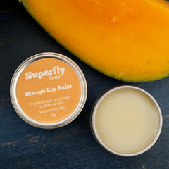 Lip balm tin with orange label, silver metal, and yellow balm inside, with mango fruit