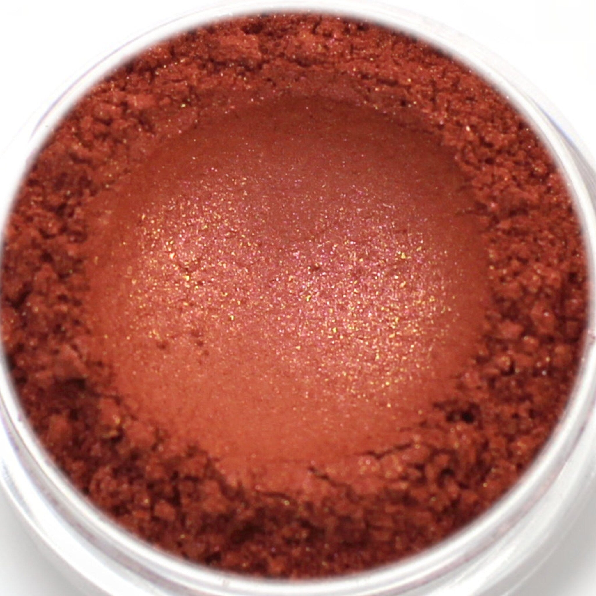 Eyeshadow powder in reddish-brown color with glitter particles and a powdery texture in a clear container