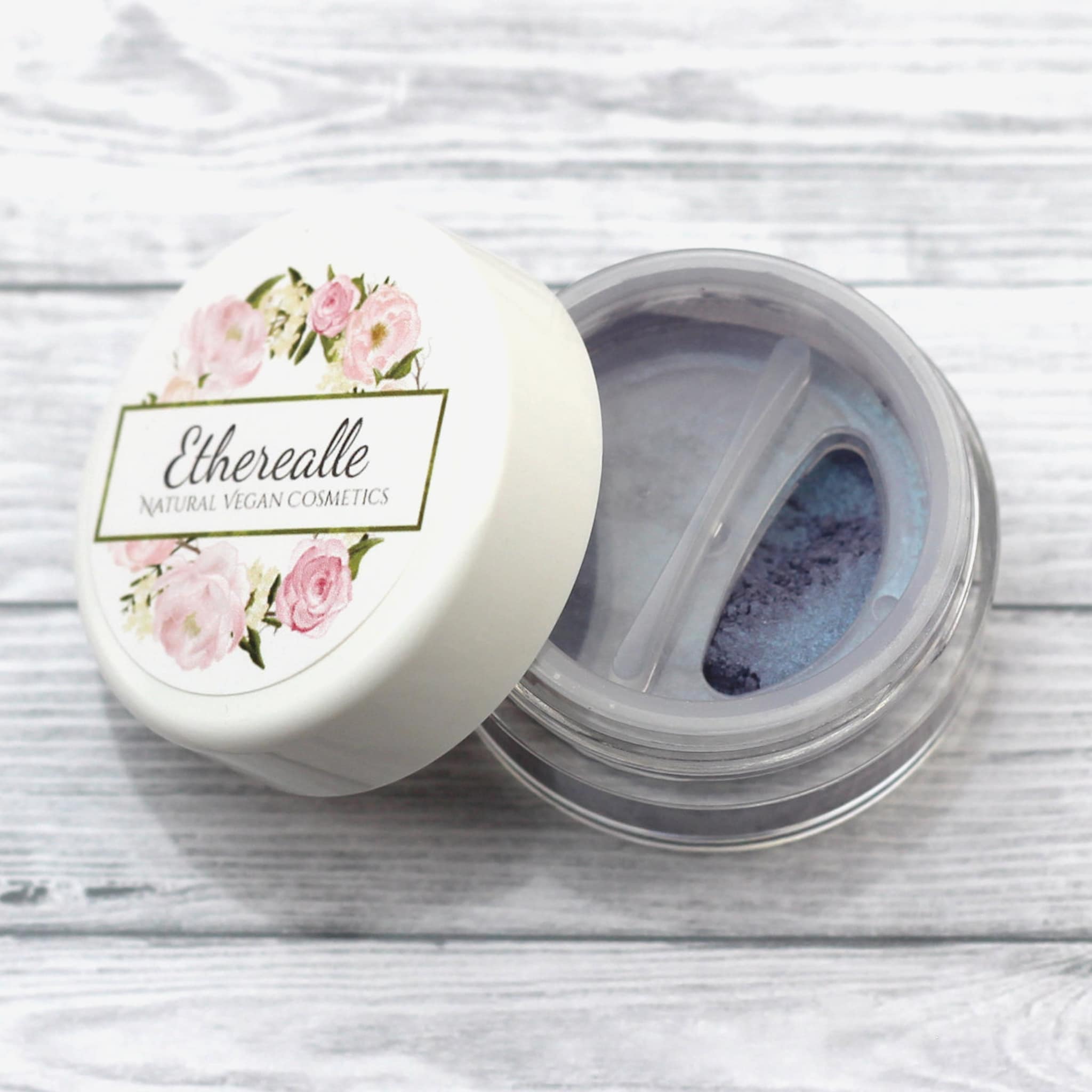 Etherealle powder eyeshadow in blue and purple shades, white lid with floral design, clear jar
