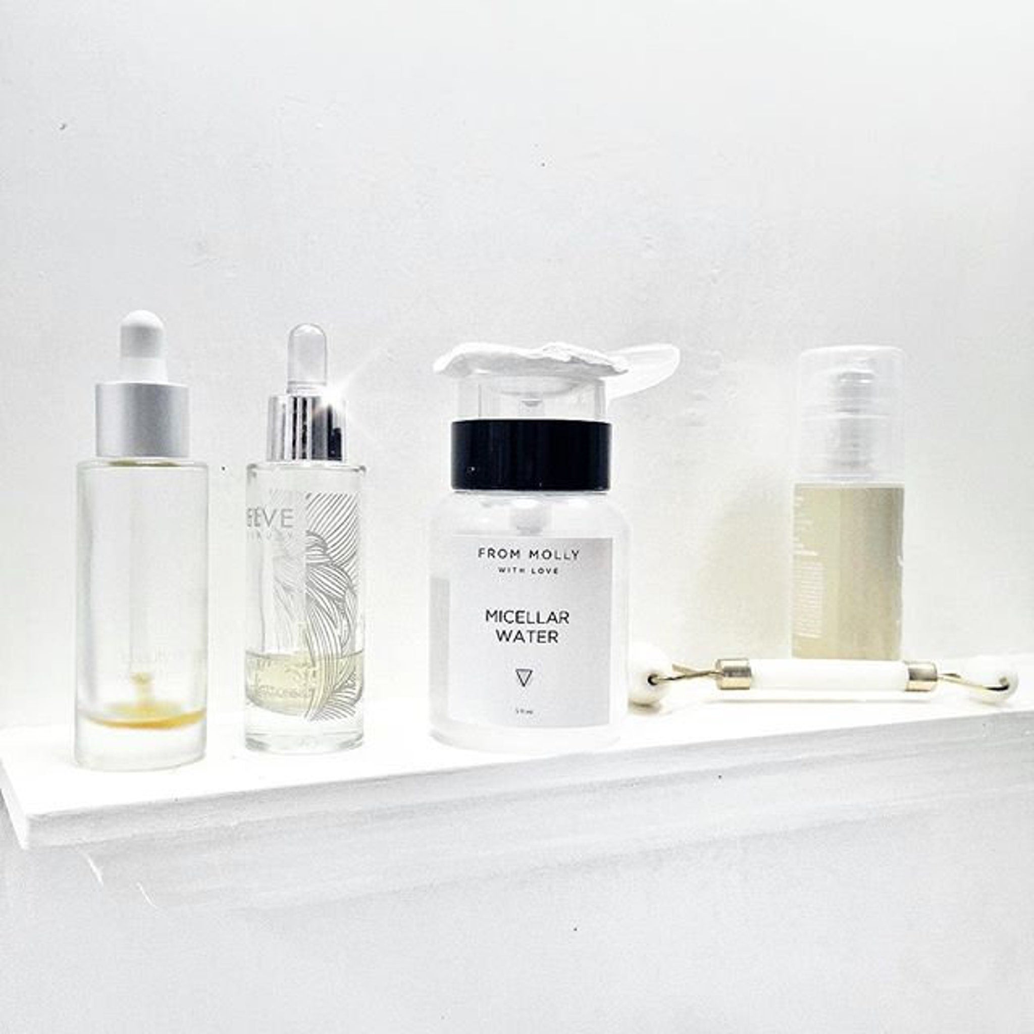Skincare products in clear, glass bottles with white and silver caps, on a white shelf