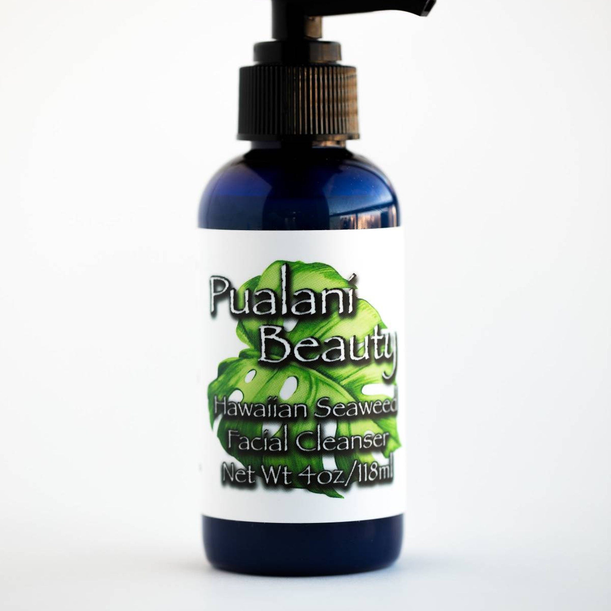 Facial cleanser bottle, dark blue glass, white label, black pump top, Pualani Beauty brand