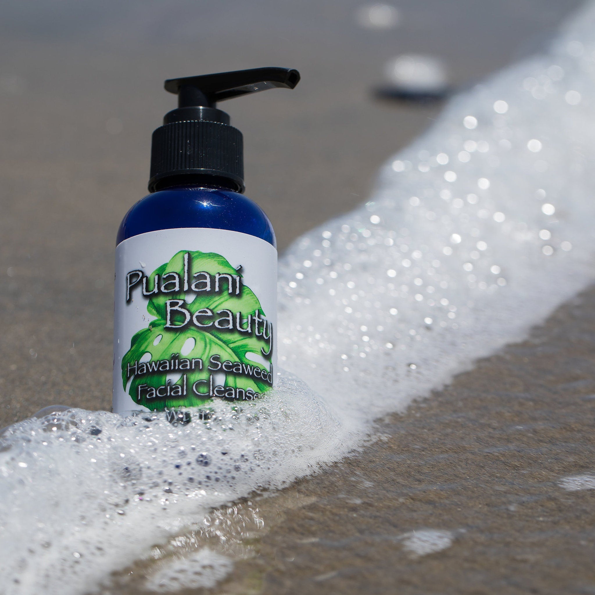Facial cleanser bottle, blue and white label, black pump, Pualani Beauty brand, in foamy water