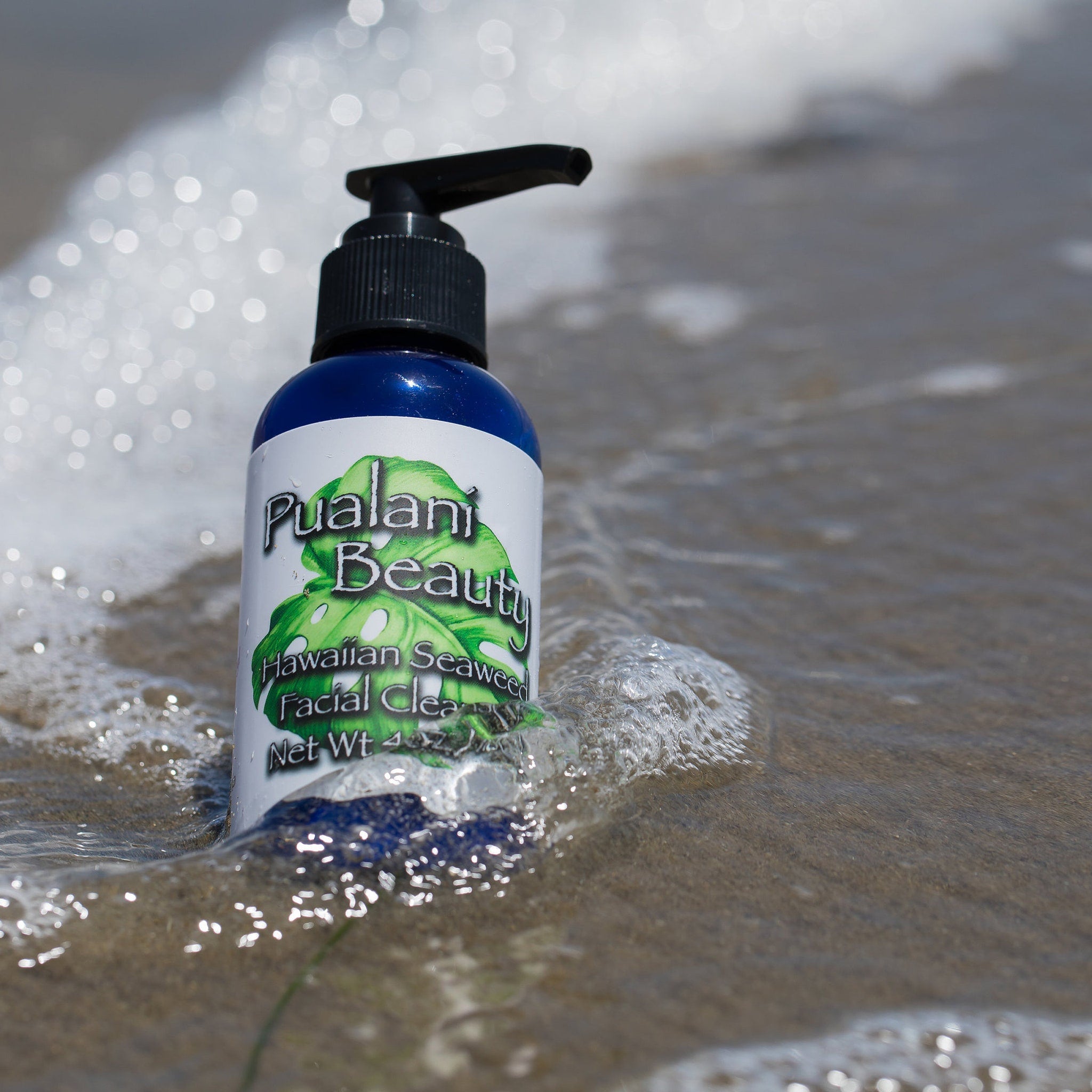 Facial cleanser bottle with blue and white label, black pump, in ocean water with Pualani Beauty text