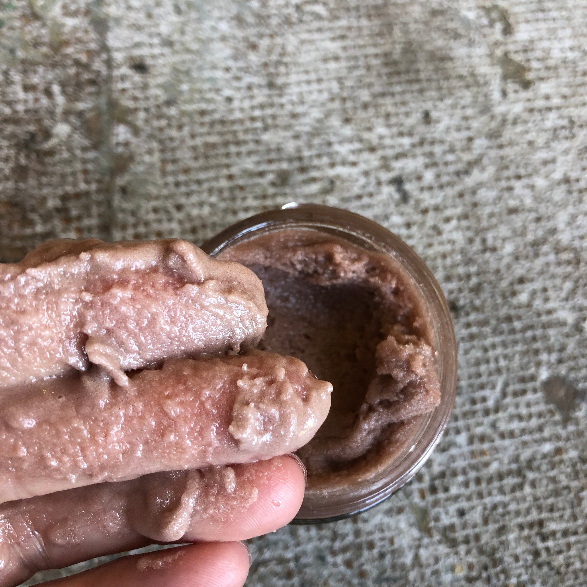 Body scrub with pinkish brown color, creamy texture, and glass jar container on hand