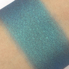Eyeshadow swatch in teal blue with a textured, grid-like pattern on skin