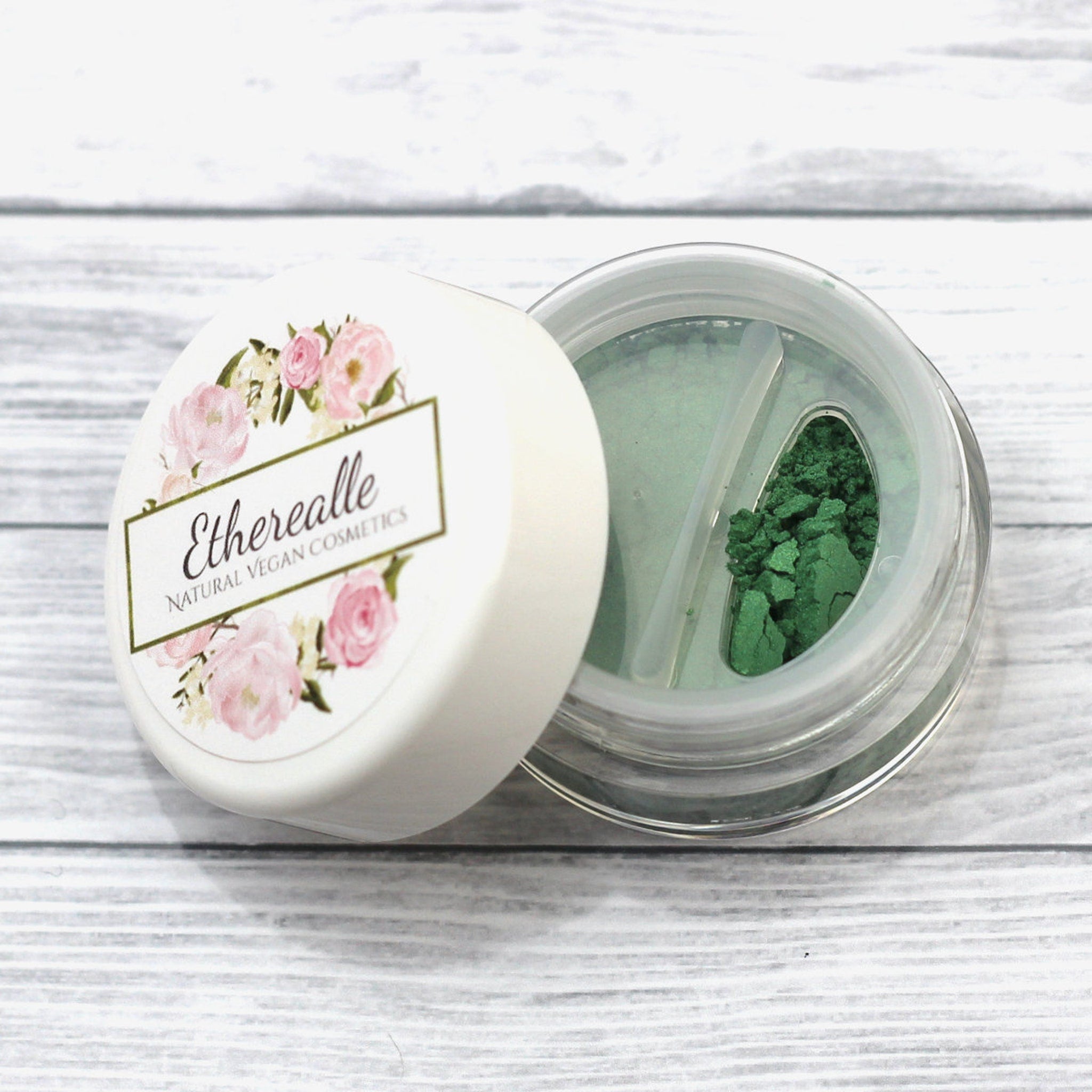 Etherealle green eyeshadow in a clear container with floral lid and white background