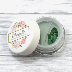 Etherealle green eyeshadow in a clear container with floral lid and white background