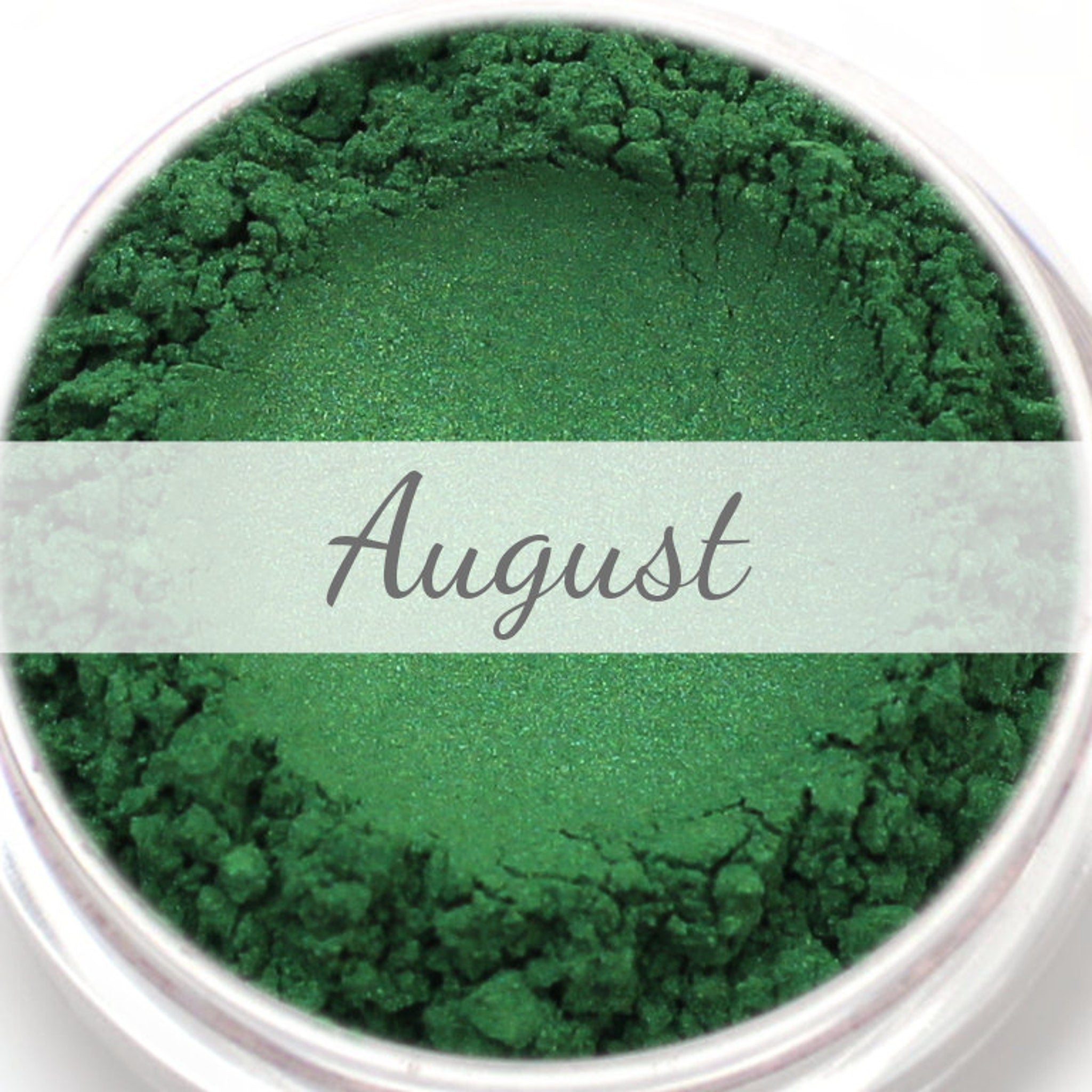 Green powder with "August" text, in a clear container, close-up view