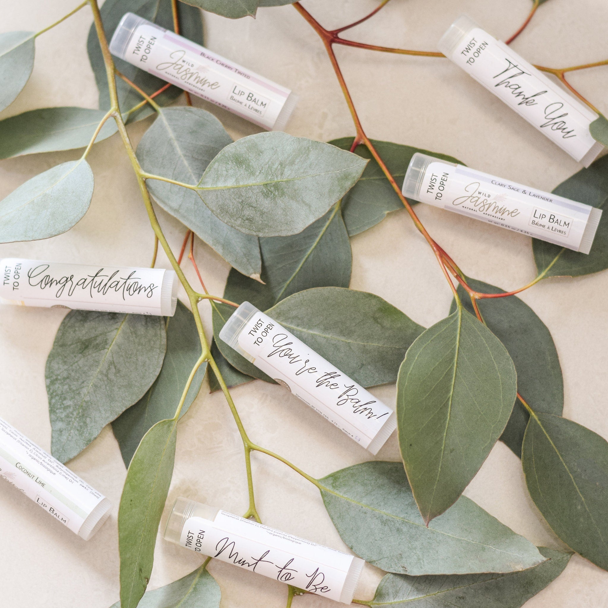 Lip balm tubes with white and light green labels, eucalyptus leaves, Wild Jasmine Apothecary brand