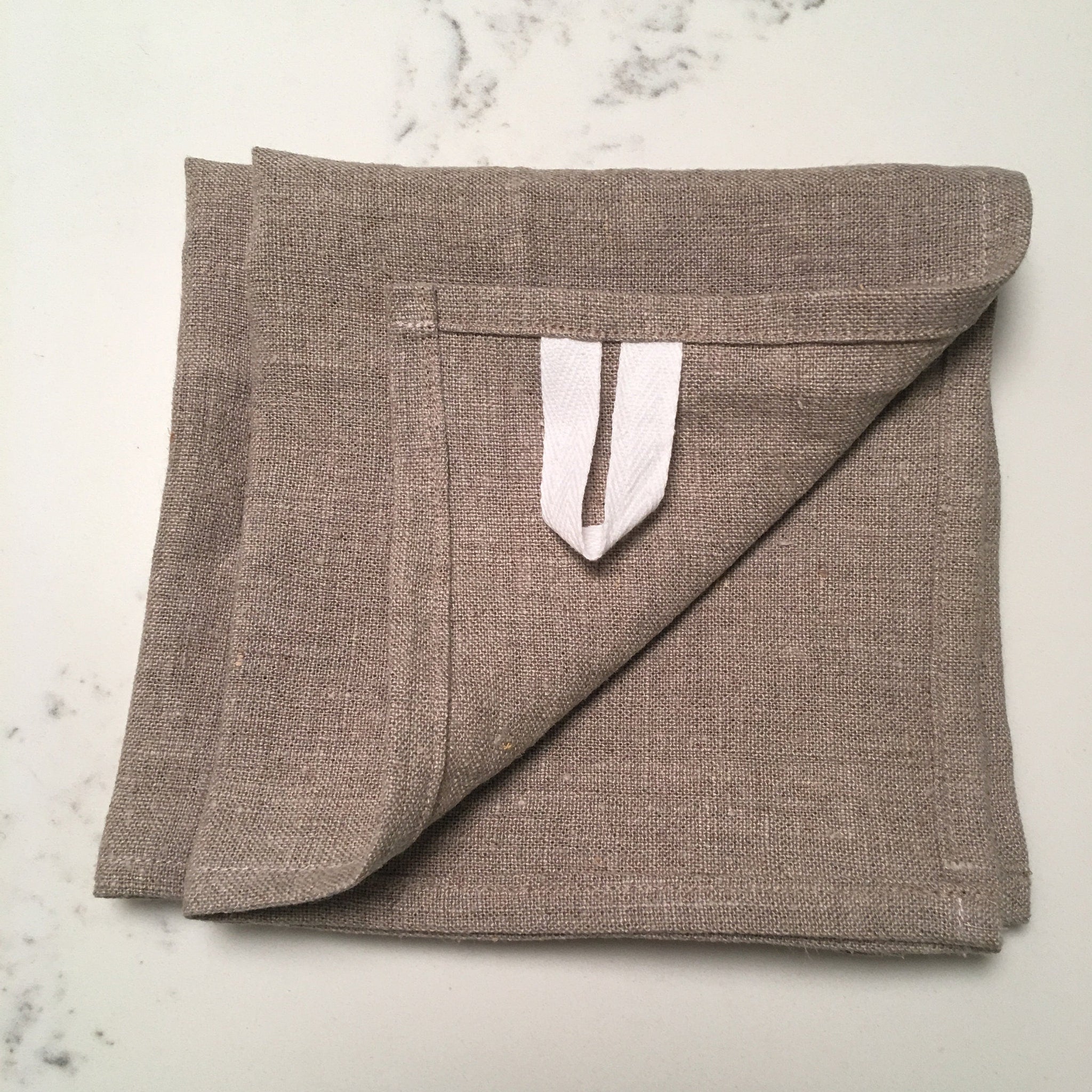Linen towel in tan color, woven material, folded with white hanging loop detail