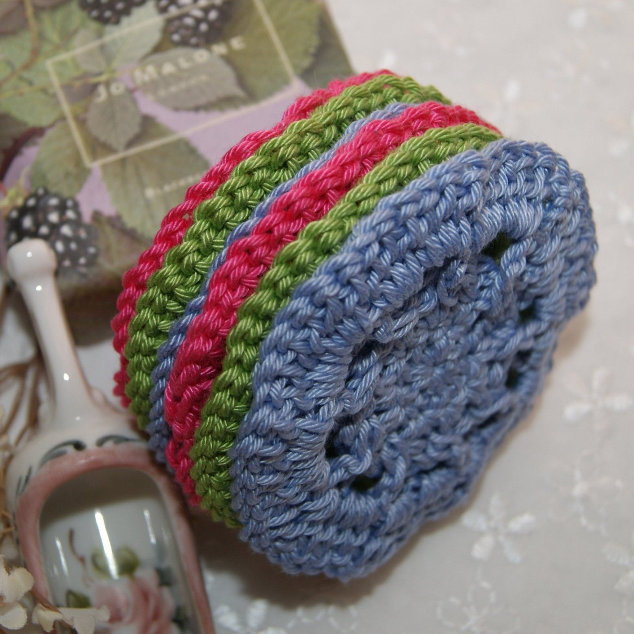 Crochet coasters in blue, pink, and green yarn, stacked together on a white surface