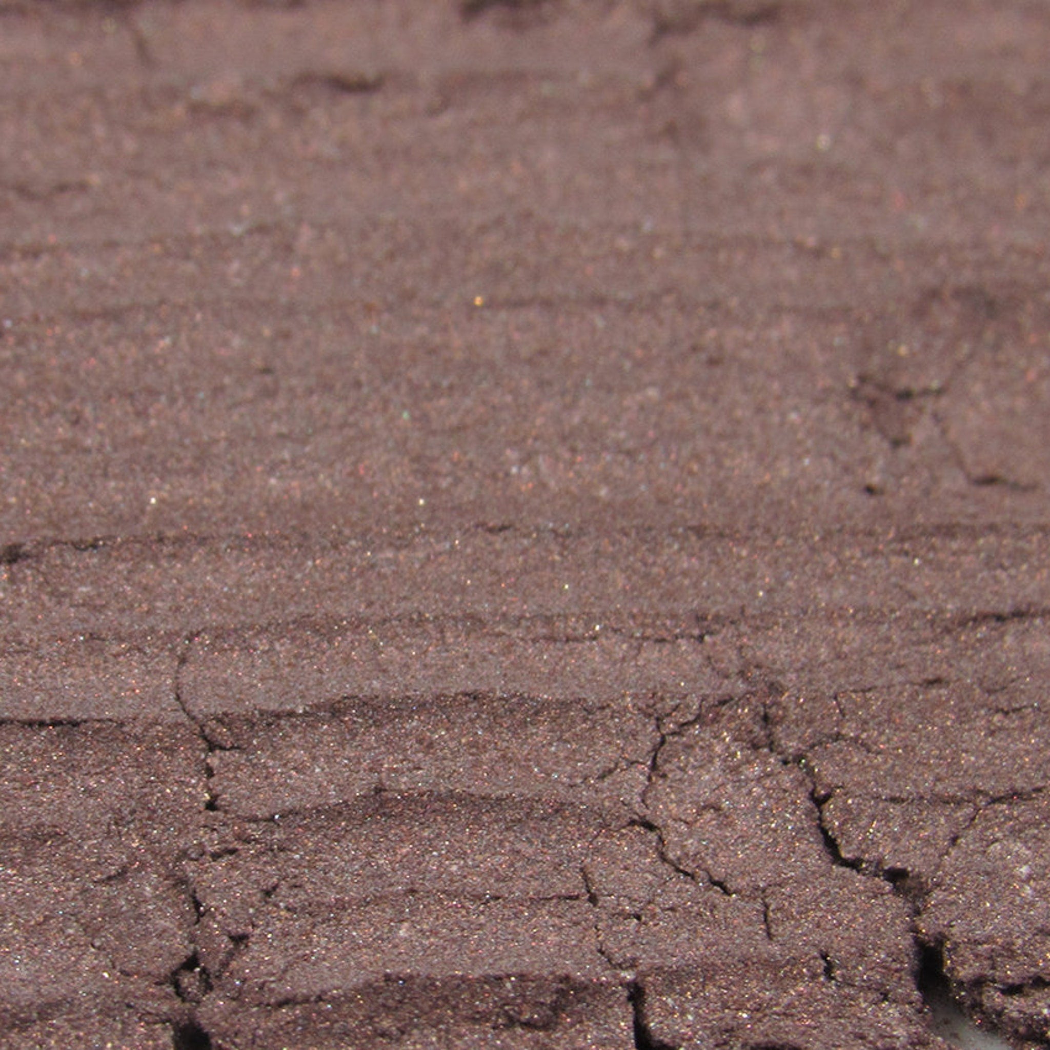 Brown eyeshadow with shimmer, textured surface, and cracked appearance.