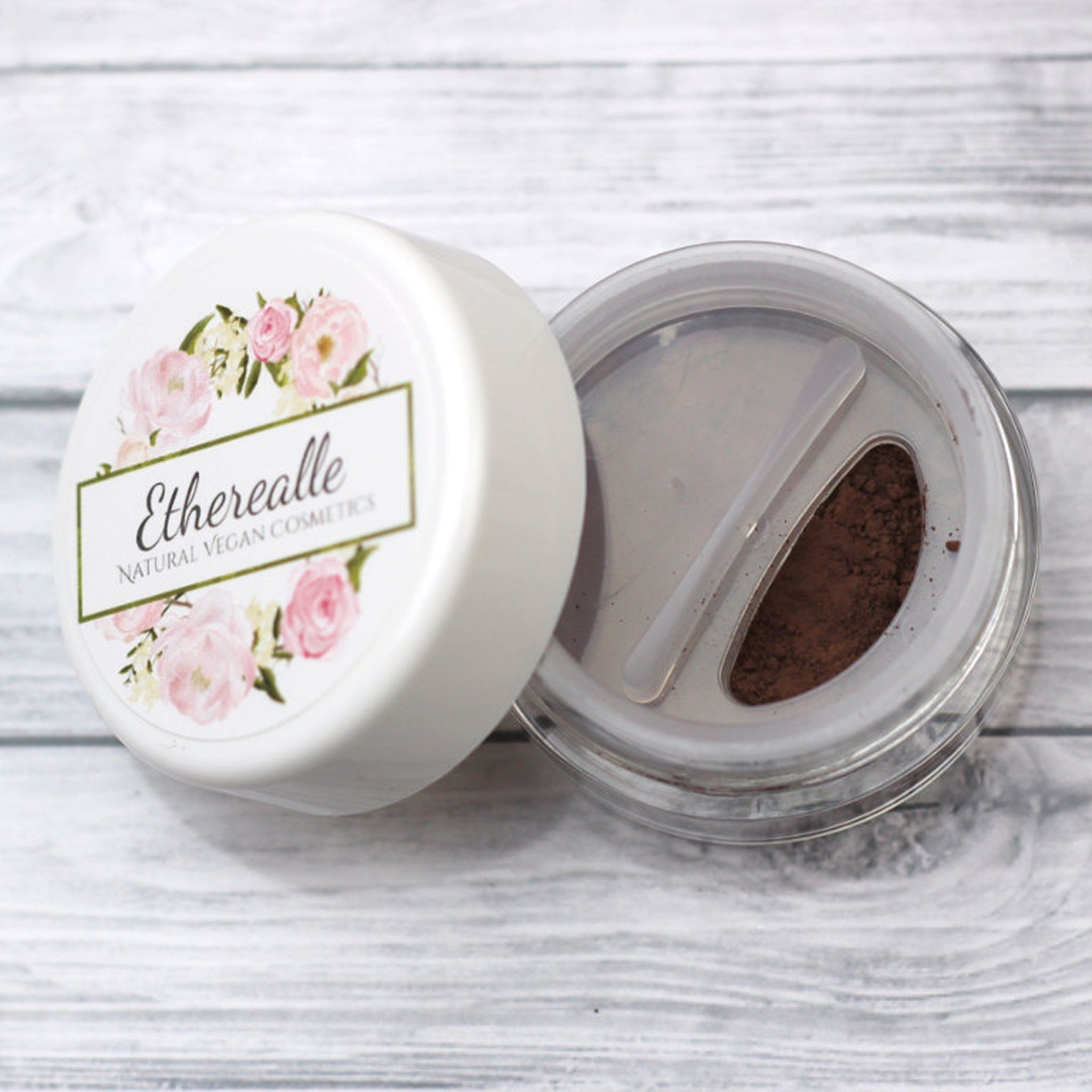 Cosmetic powder in white container with floral design and brand name Etherealle, brown powder visible