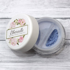 Hand applying vegan mineral eyeshadow in shimmering blue with pink and turquoise flecks to eyelid
