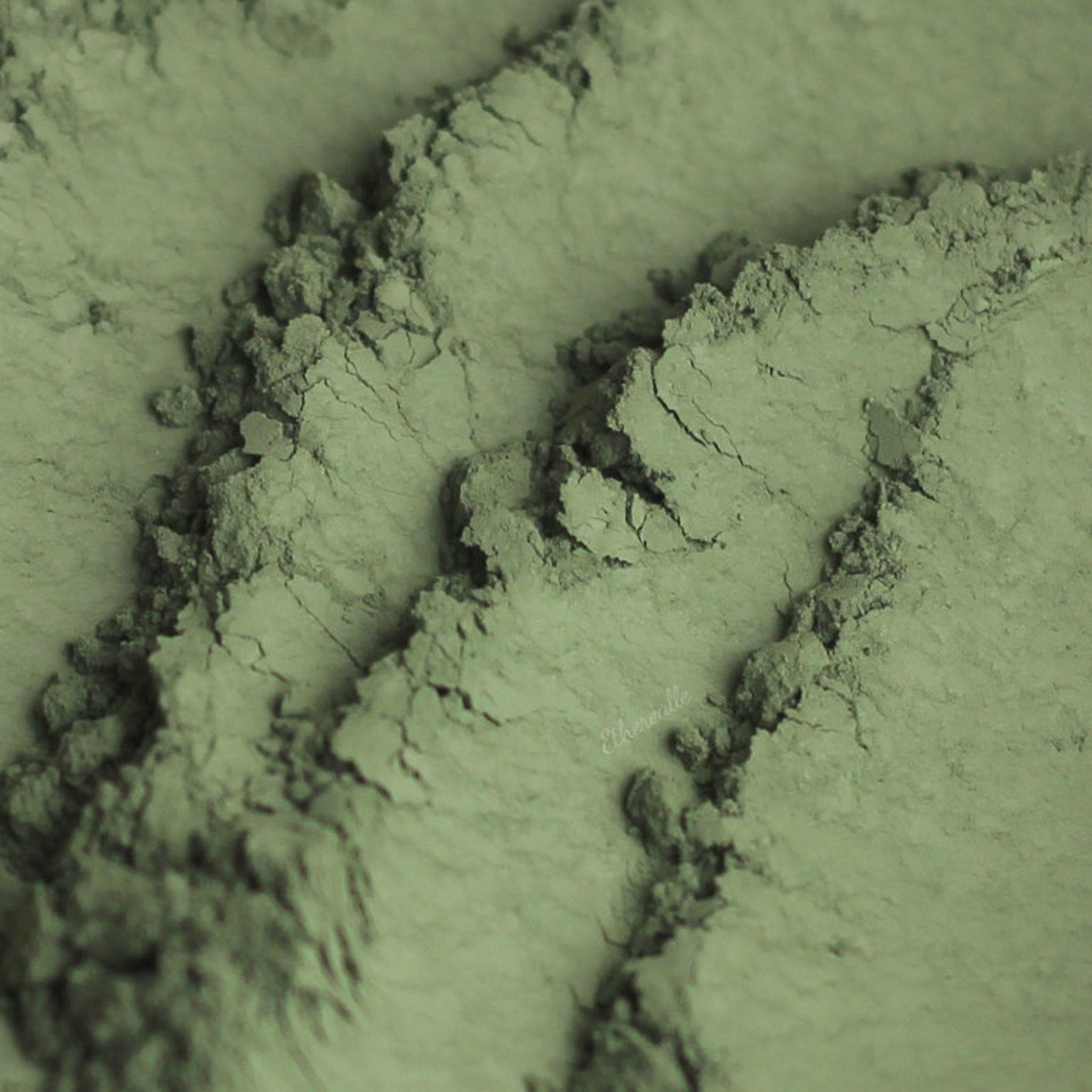 Close-up of matte khaki green eyeshadow being applied to eyelid with a fluffy brush