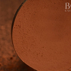 Side view of matte pressed eyeshadow single pan in chic orange and brown tones, showcasing texture and compact shape