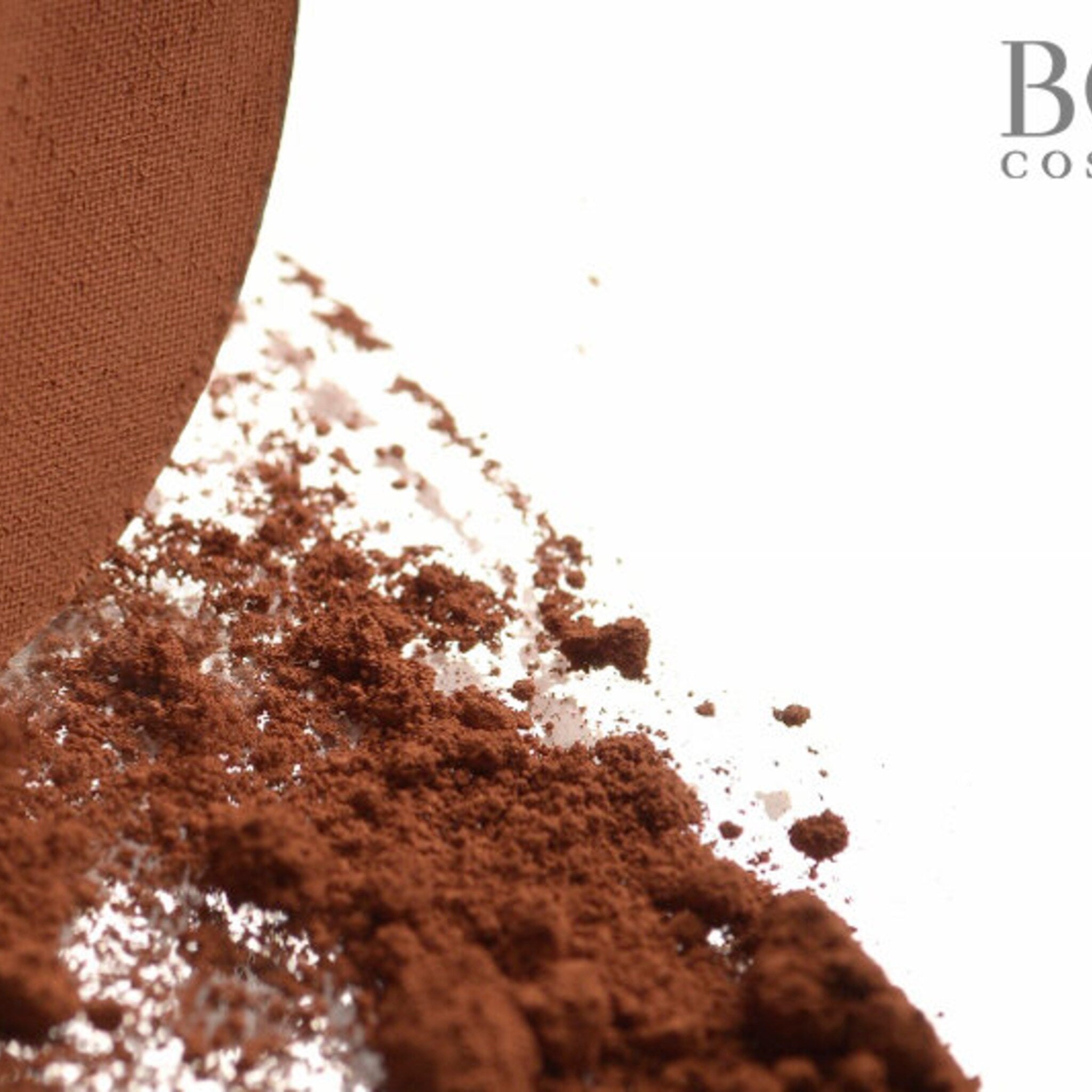 Close-up of fingertips applying matte orange-brown eyeshadow to eyelid with blending brush