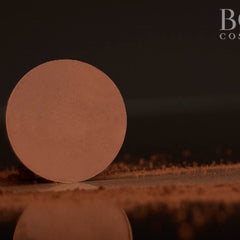 Brown powder compact with a circular shape and textured surface, reflected on dark surface