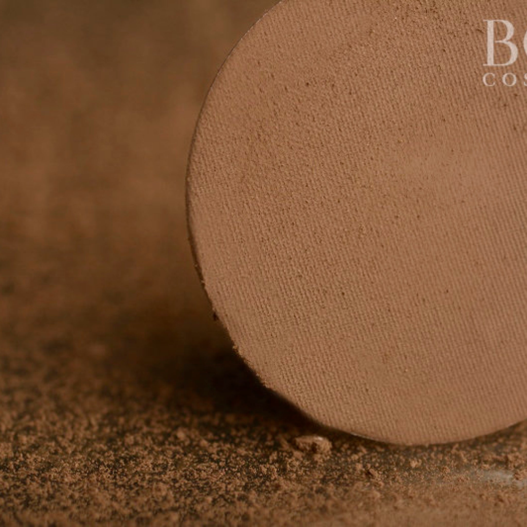 Powder compact with brown color and textured surface, with "B" brand text visible