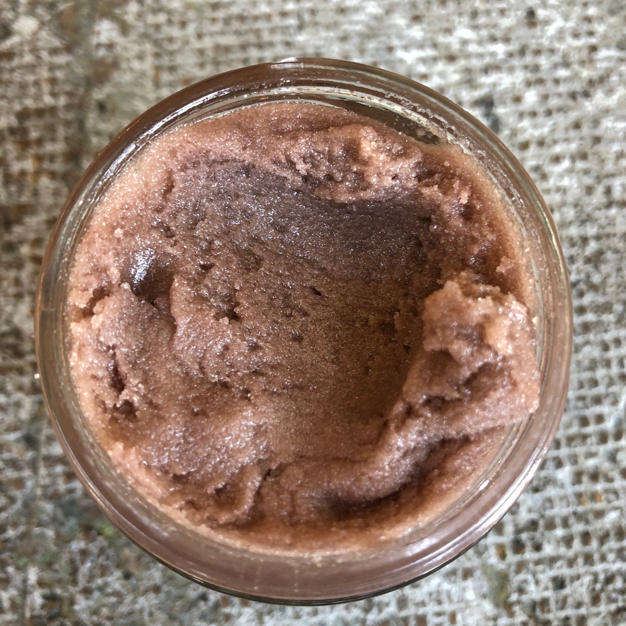 Body scrub in glass jar, brown and pink, textured, top-down view