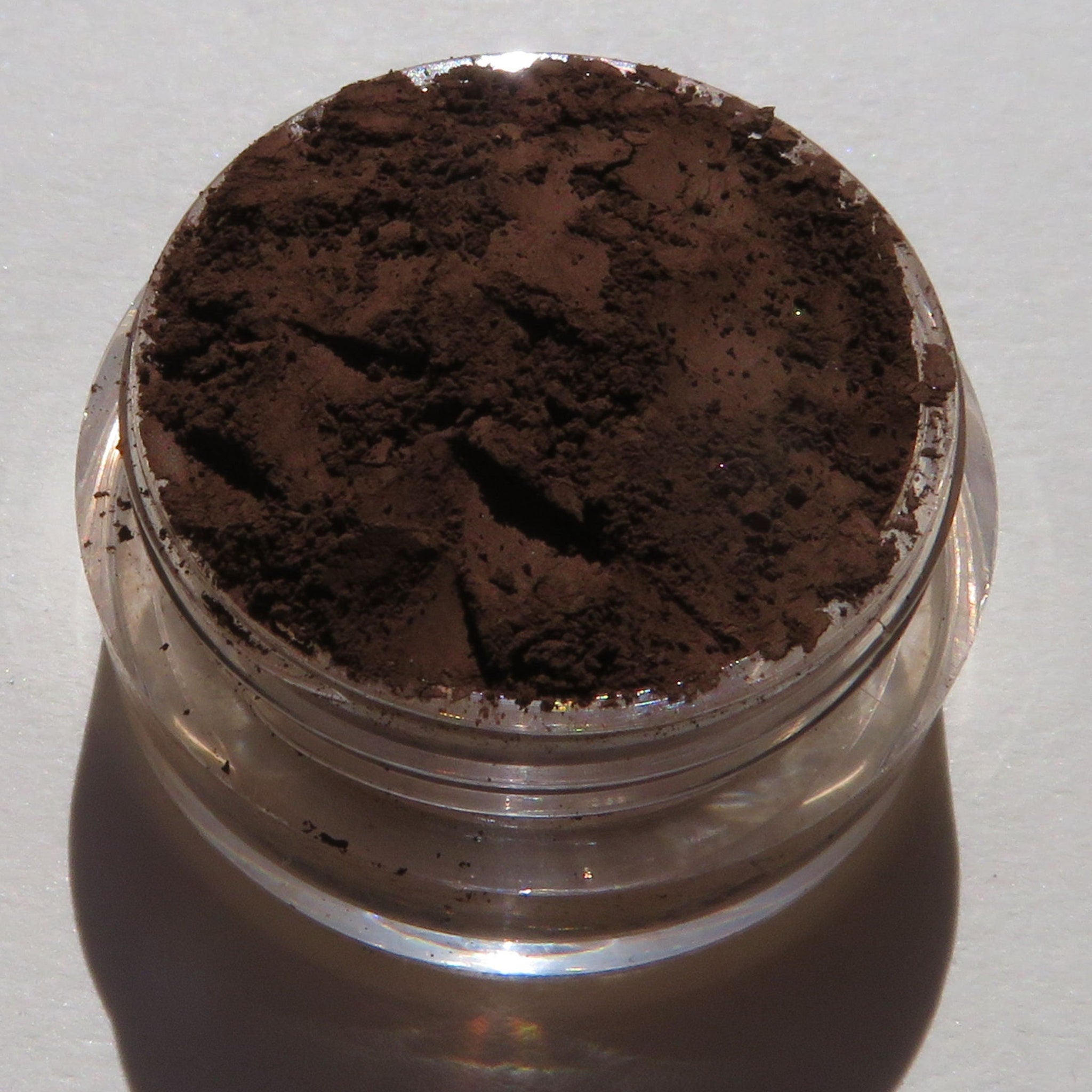 Side view of matte brown mineral eye shadow in loose powder form with vegan labeling on compact