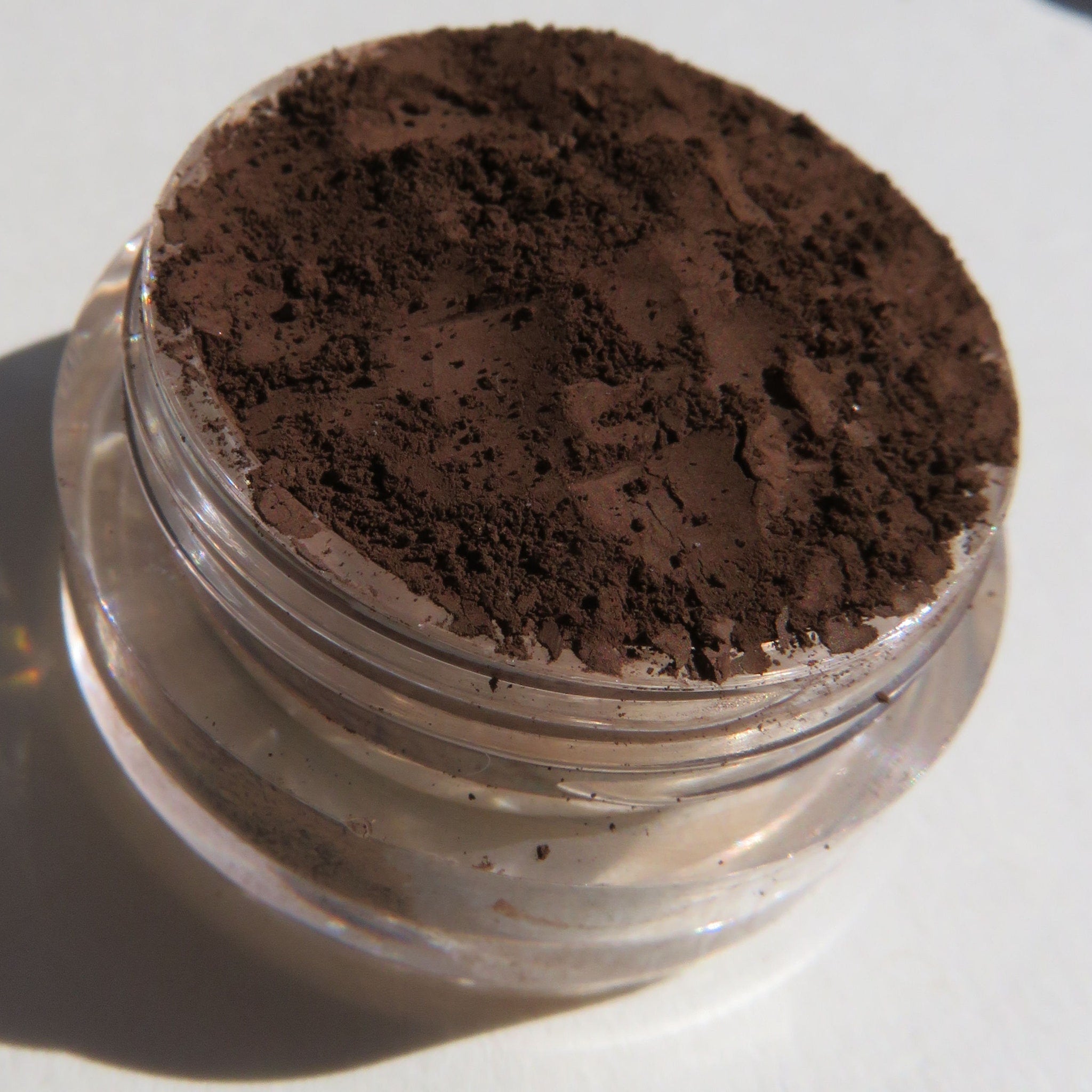 Side view of matte brown mineral eye shadow powder in open jar with loose texture and vegan label visible