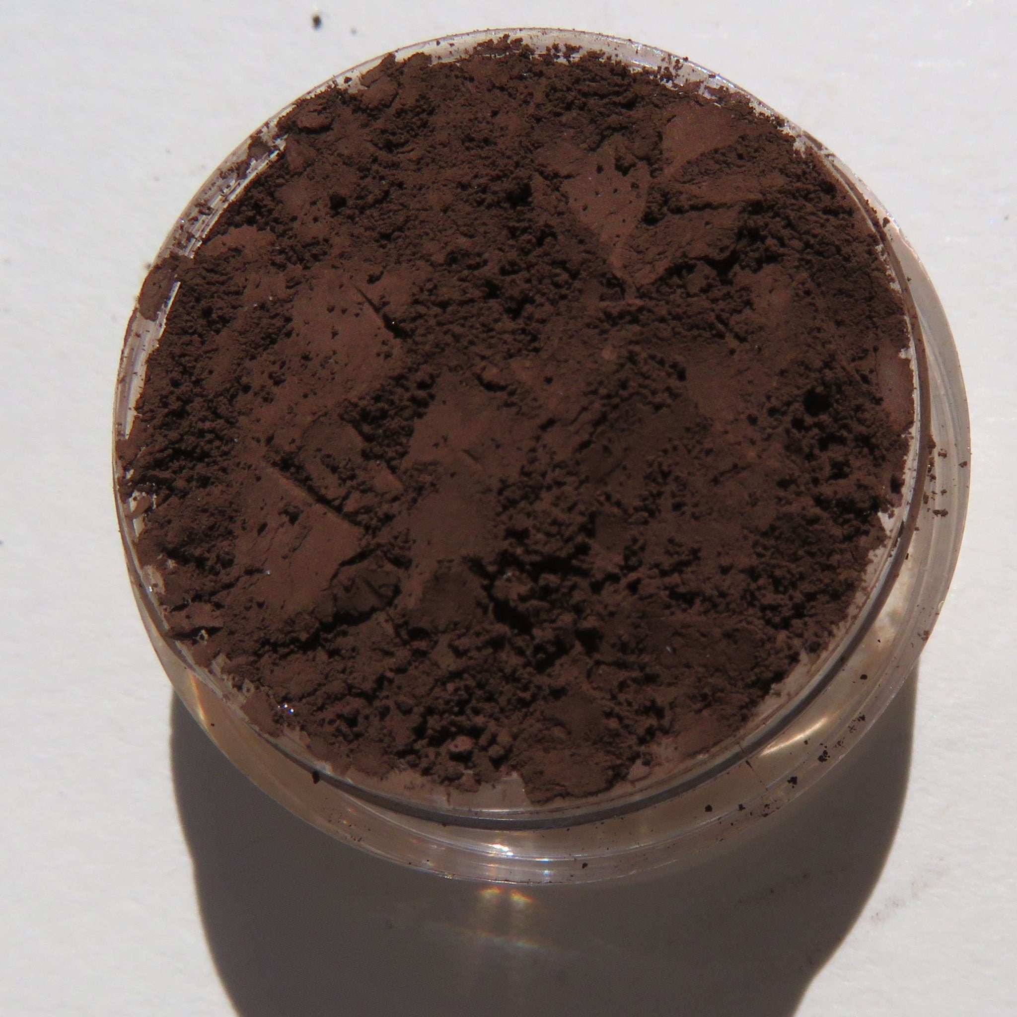 Matte brown mineral eye shadow pot with vegan loose powder spilling onto marble surface
