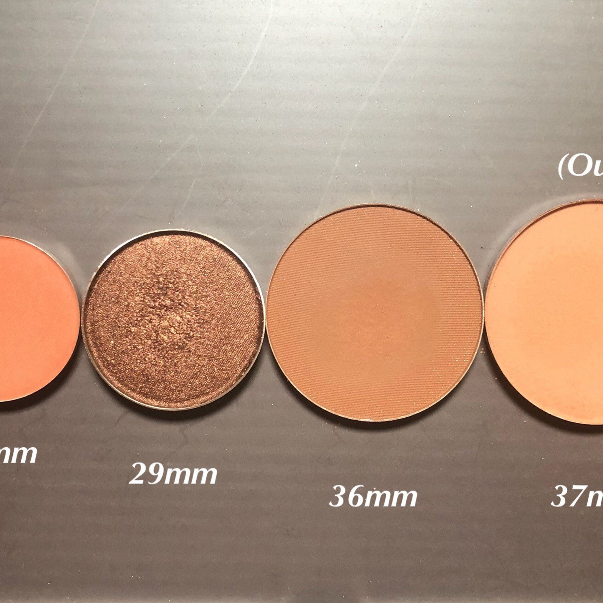 Eyeshadow pans in various colors and sizes, including bronze shimmer and matte peach shades