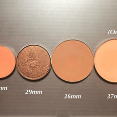 Eyeshadow pans in various colors and sizes, including bronze shimmer and matte peach shades