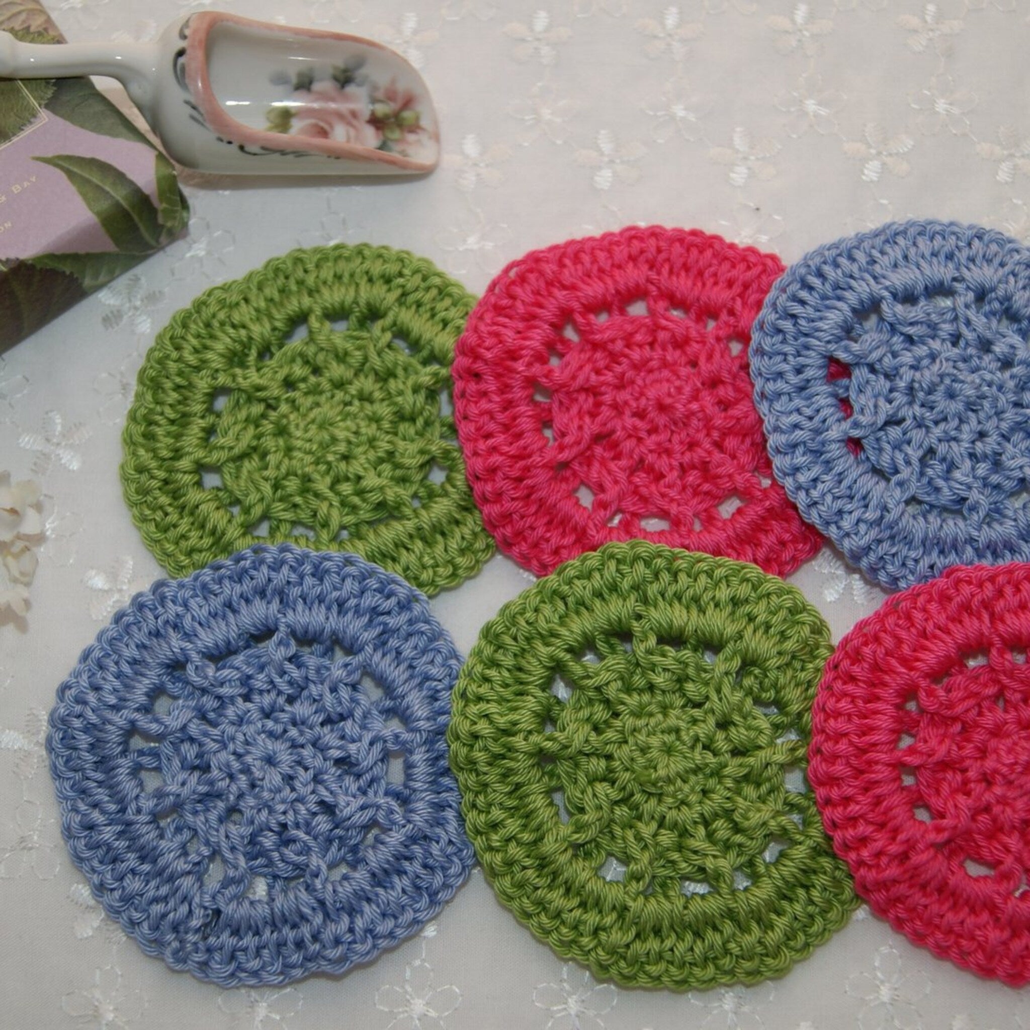 Crochet coasters in green, pink, and blue, round with openwork design