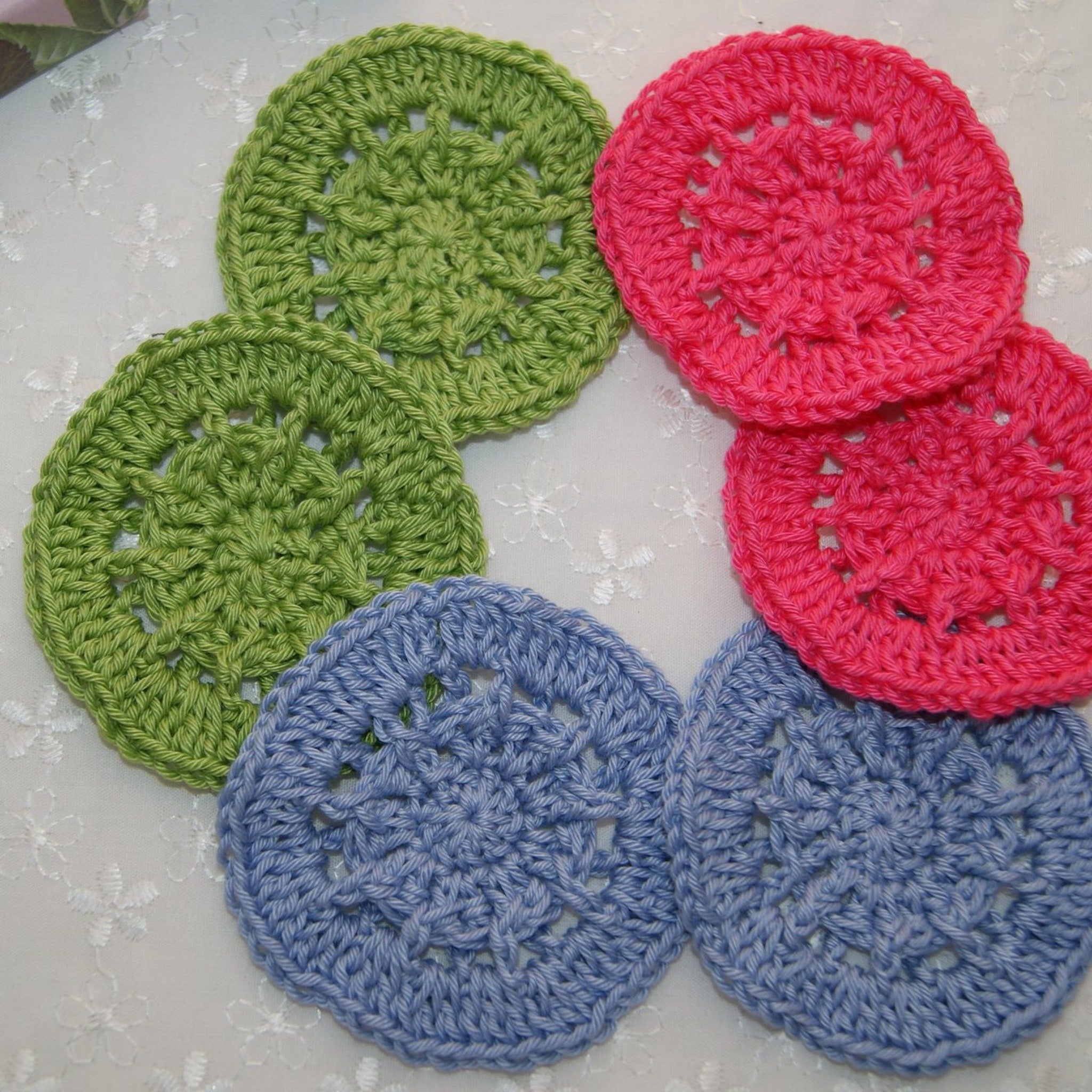 Crochet coasters in green, pink, and blue with openwork pattern on white surface