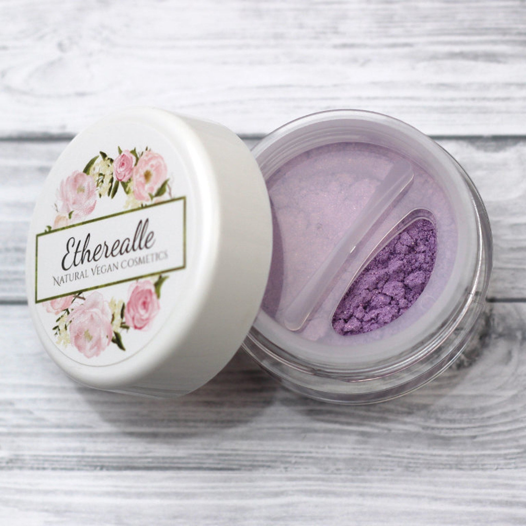 Eyelid shadow jar with white lid, pink floral design, and "Etherealle" text, open to reveal purple powder