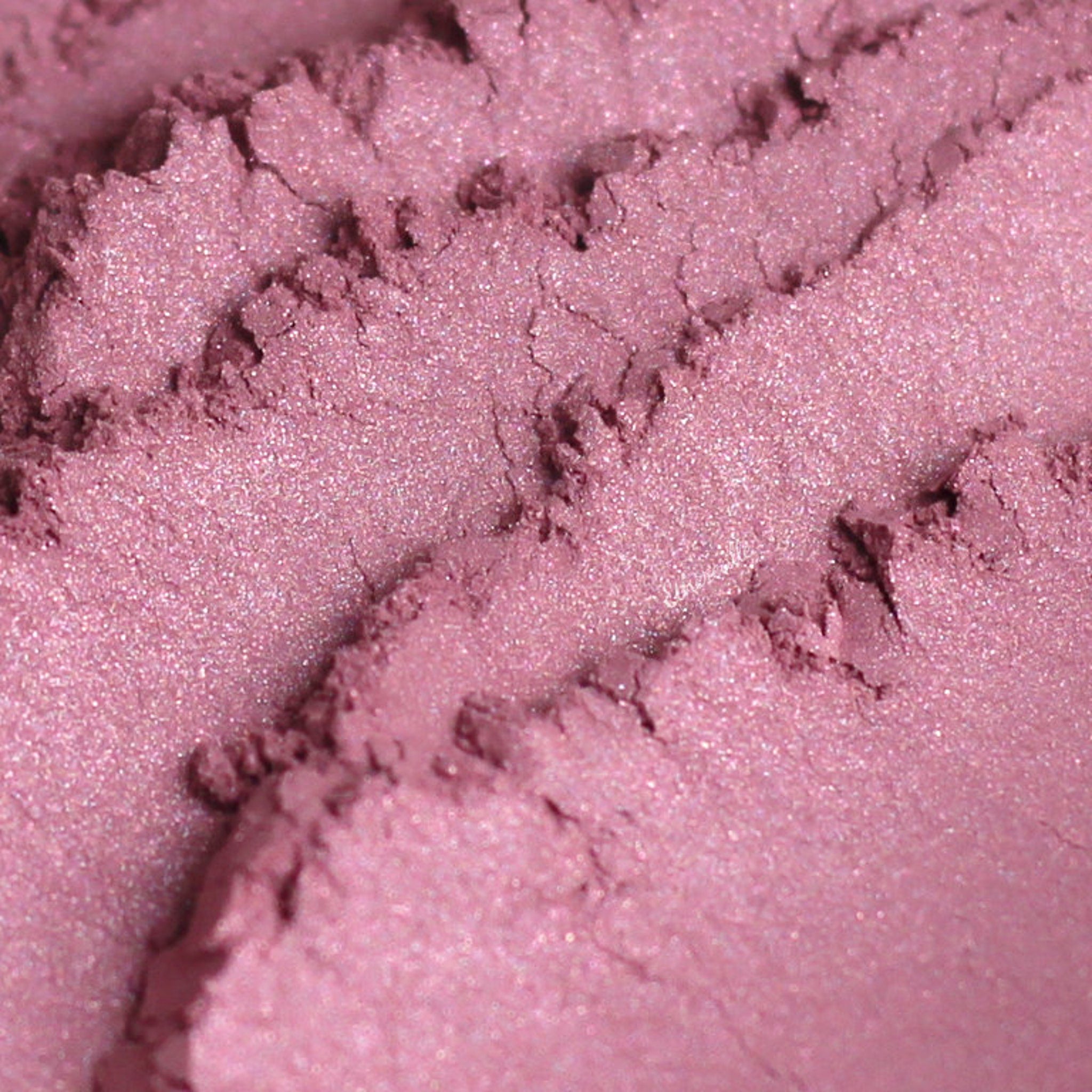 Close-up of Pixie Vegan Mineral Eyeshadow in shimmering rose pink with turquoise sparkles, showing fine powder texture.