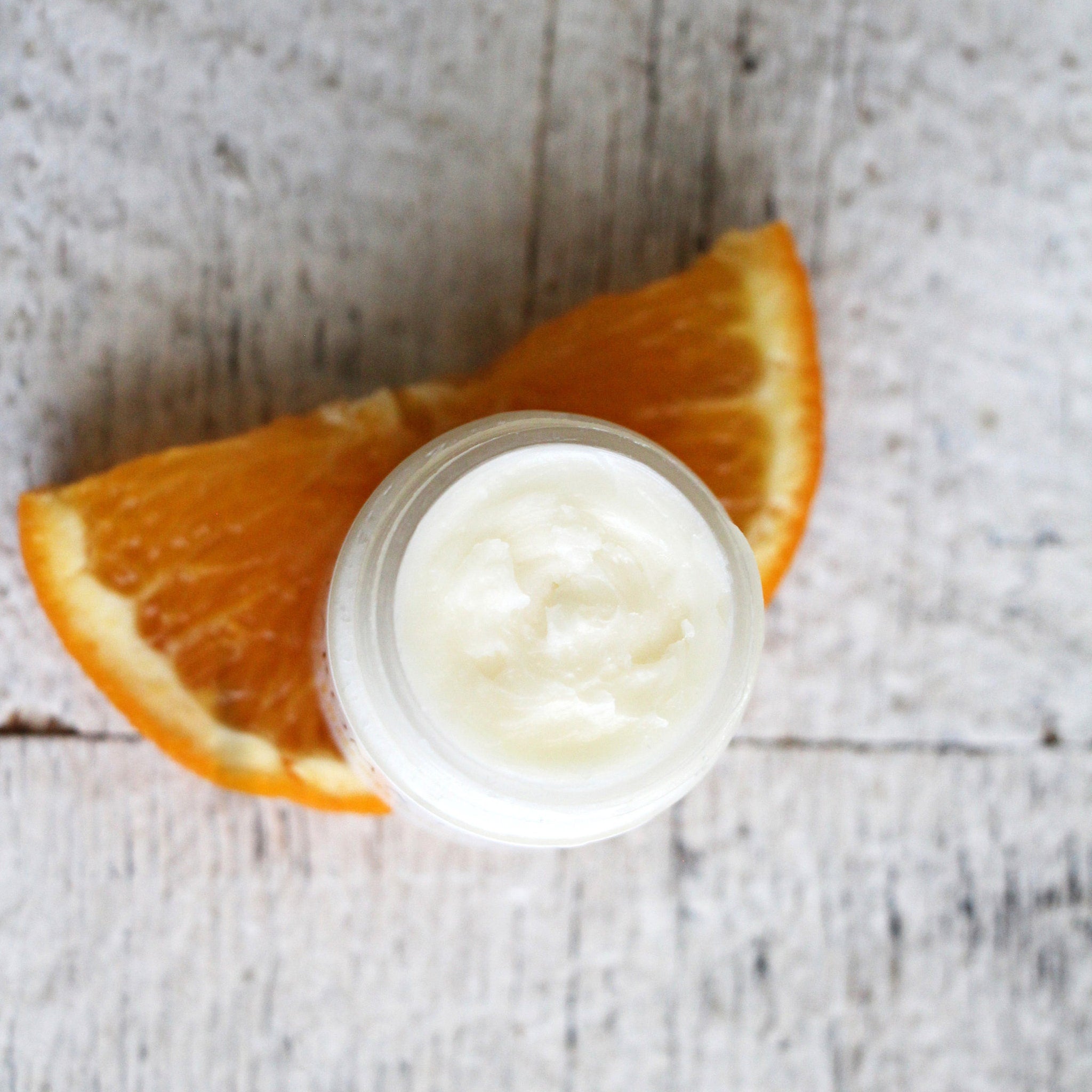 Cream jar with white cream, orange slice, and light wood background