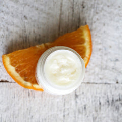 Cream jar with white cream, orange slice, and light wood background