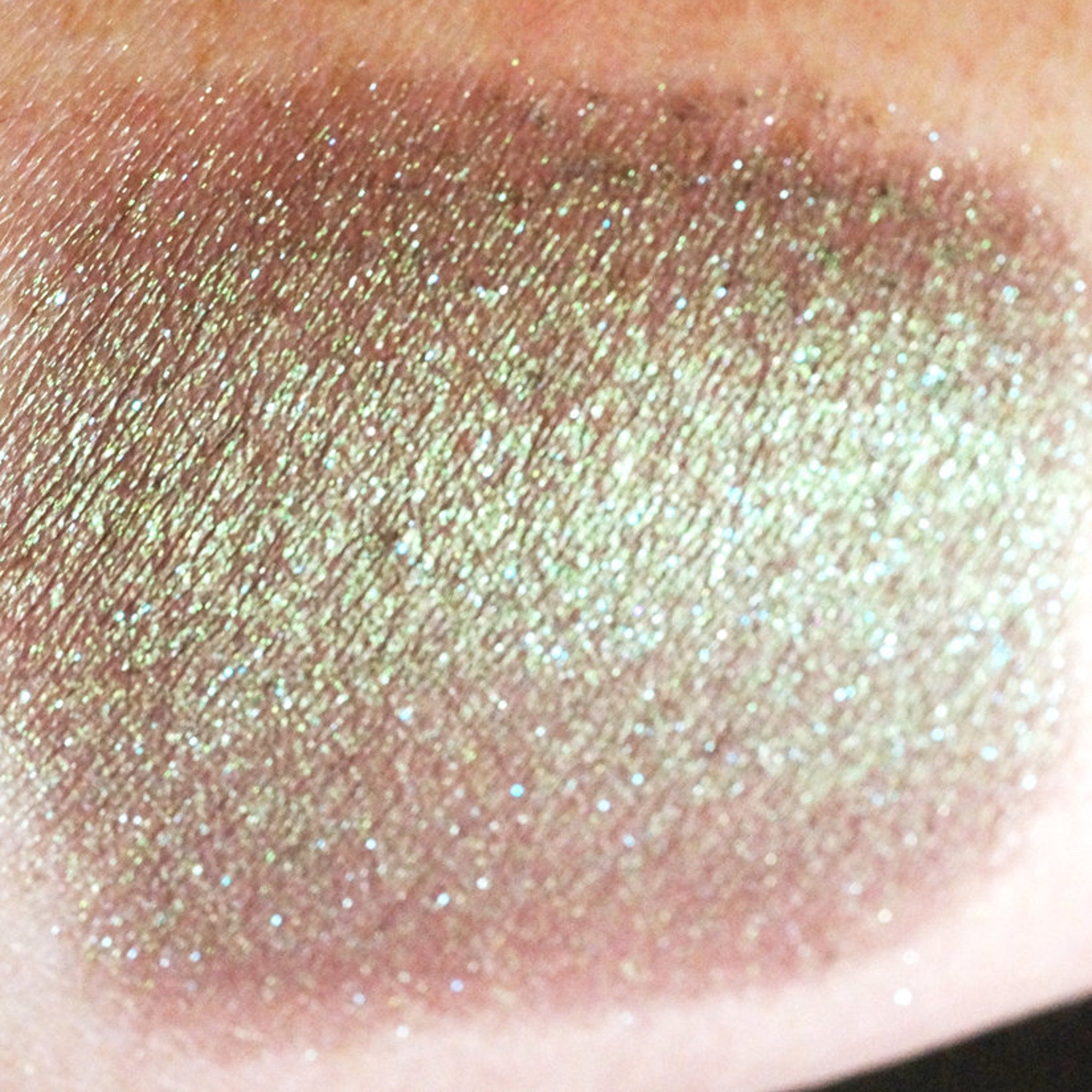 Close-up of duochrome green-brown eyeshadow pan showing iridescent shimmer shifting to burgundy in light
