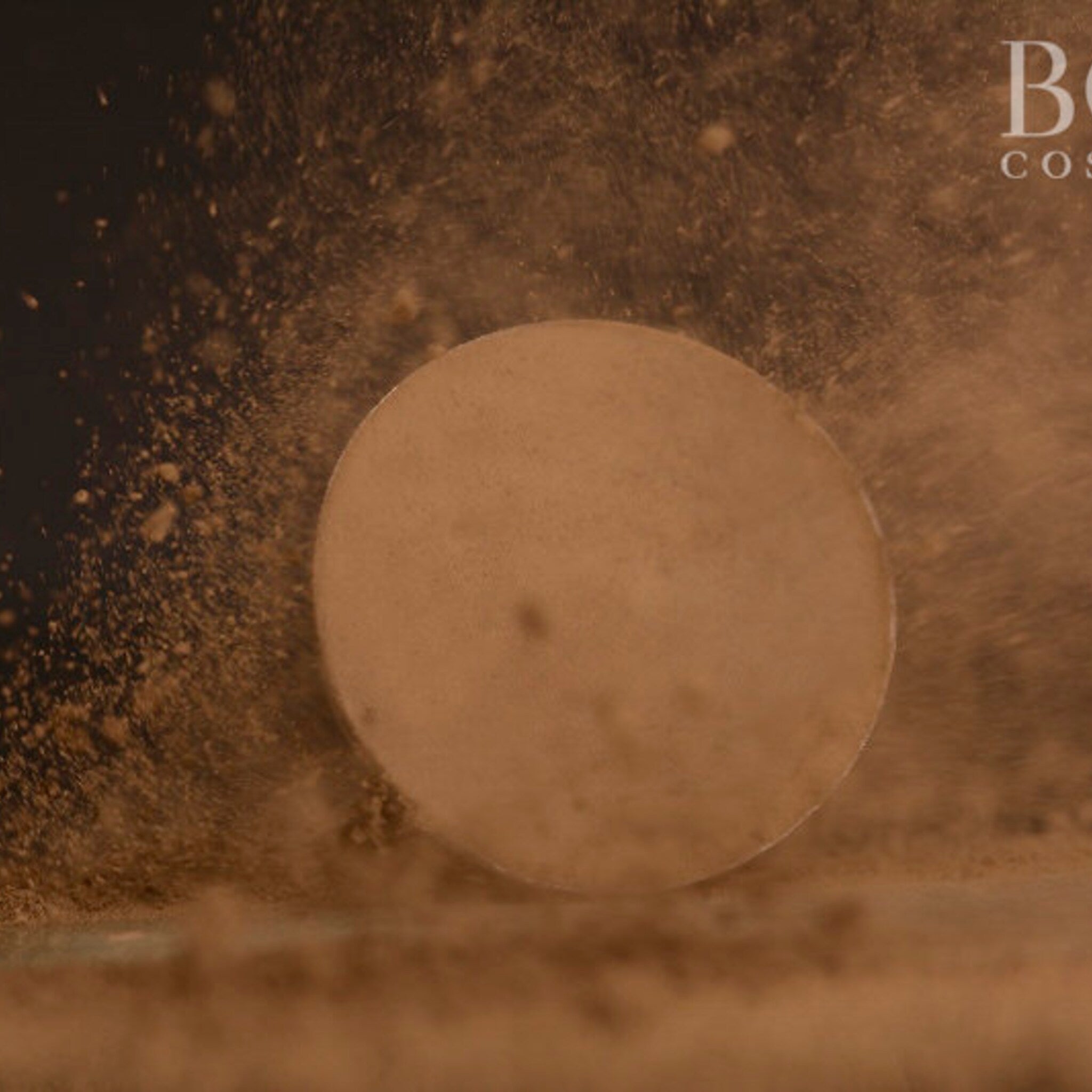 Powdered makeup product with beige color and dust particles, with "B" and "COS" text visible
