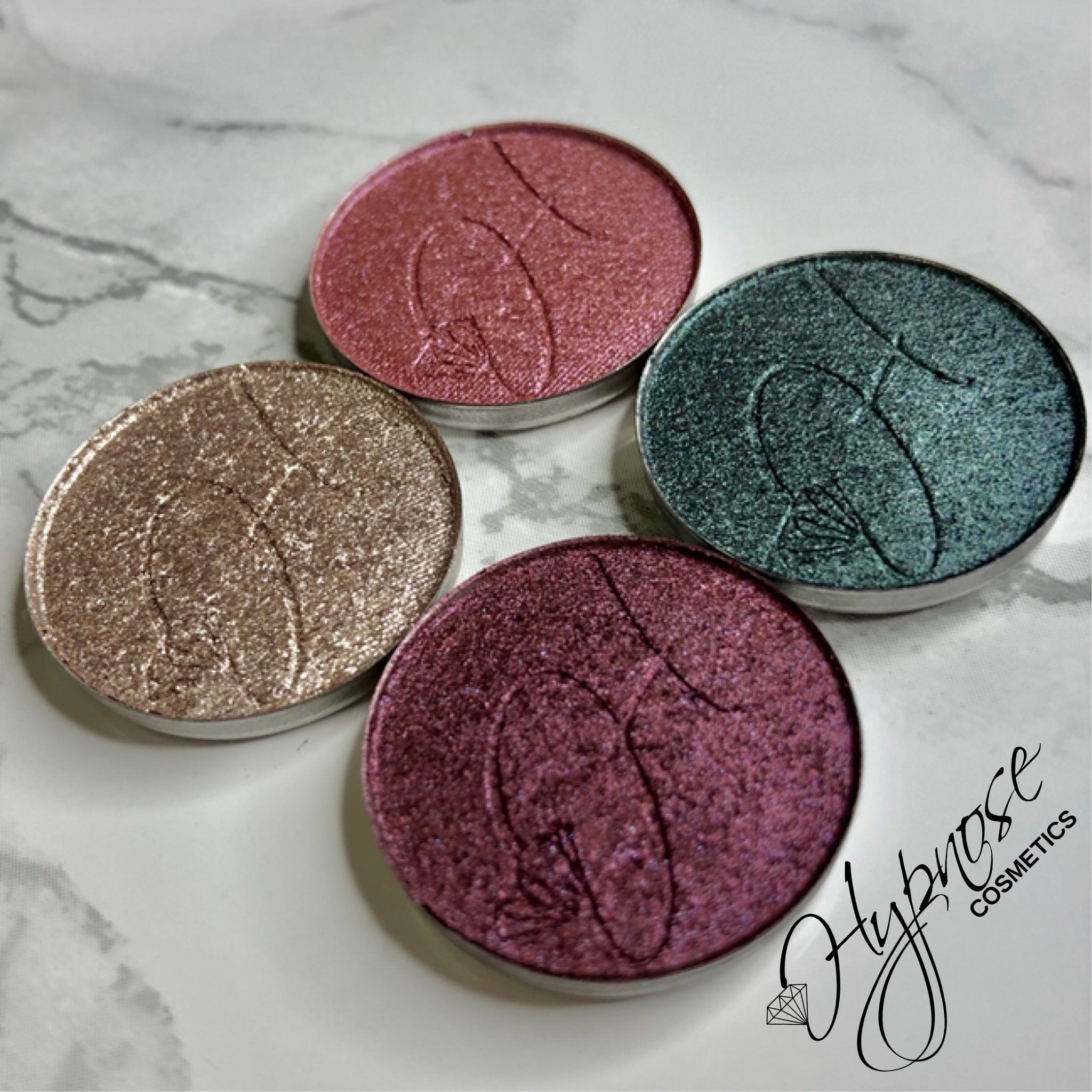 Close-up of four duochrome foiled eyeshadow pans in isotaupe, cerise, hibiscus, and peacock shades with metallic finish