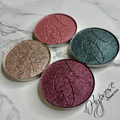 Close-up of four duochrome foiled eyeshadow pans in isotaupe, cerise, hibiscus, and peacock shades with metallic finish