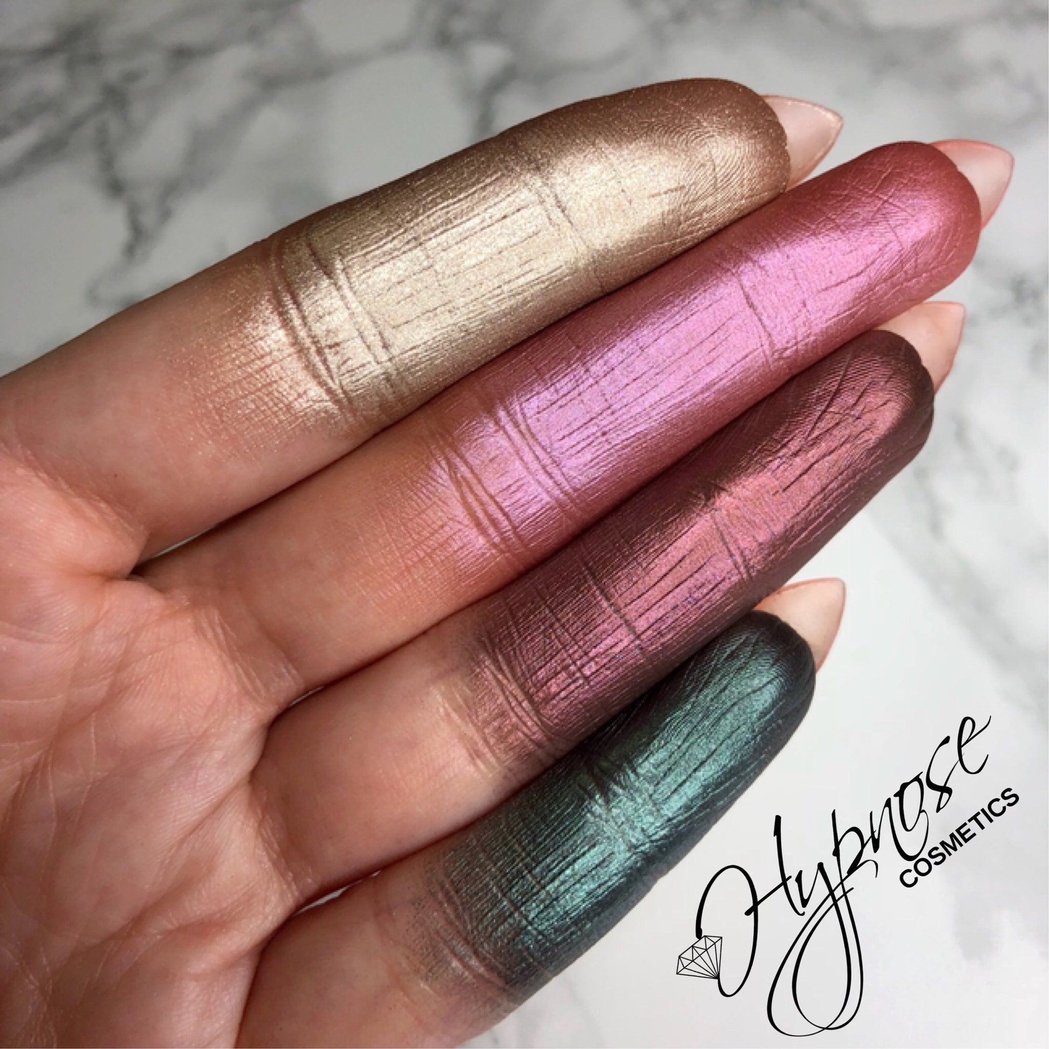 Side angle of four duochrome foiled eyeshadow pans in isotaupe, cerise, hibiscus, and peacock showing metallic sheen
