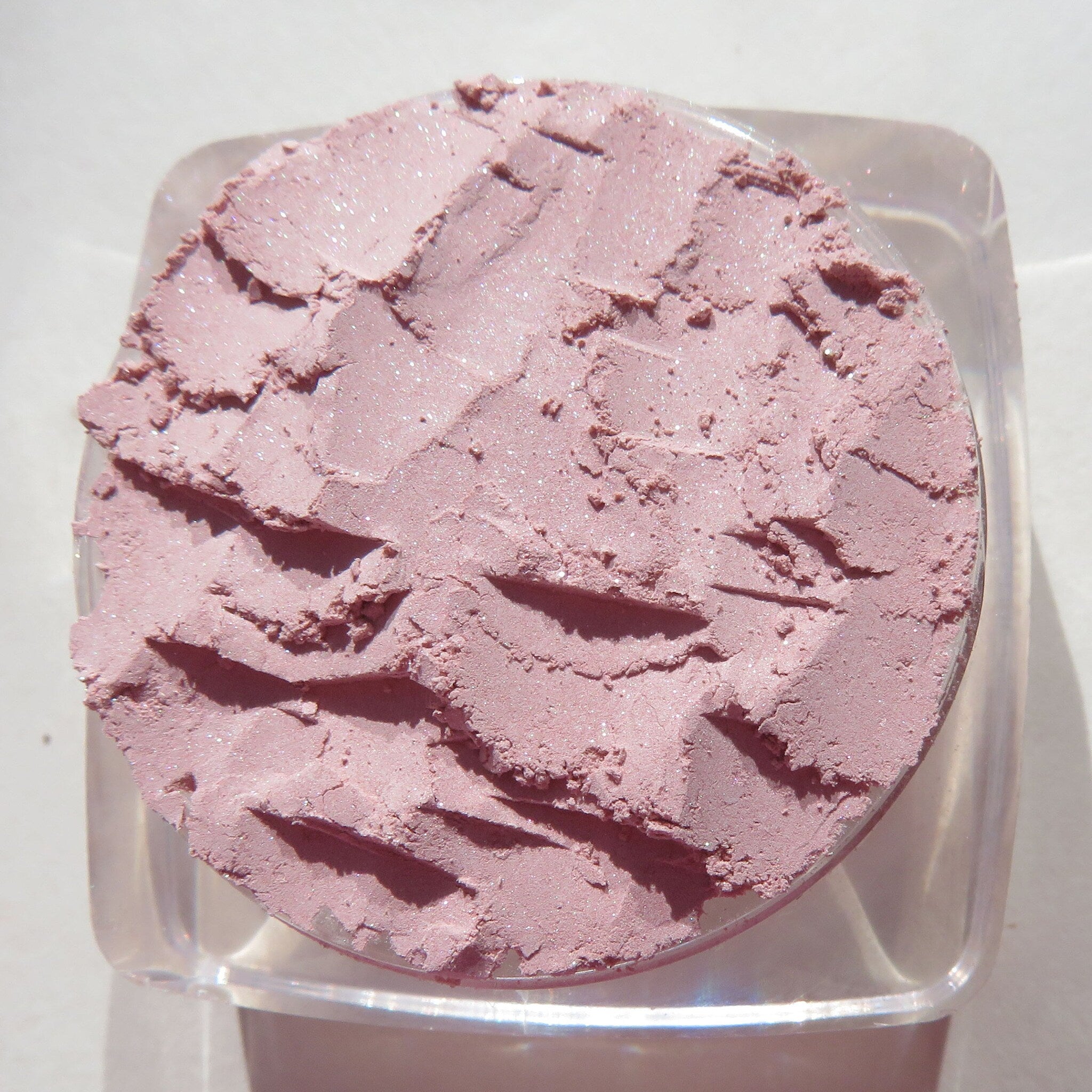 Hand applying pastel pink loose powder eyeshadow with a fluffy brush onto eyelid for soft shimmer effect