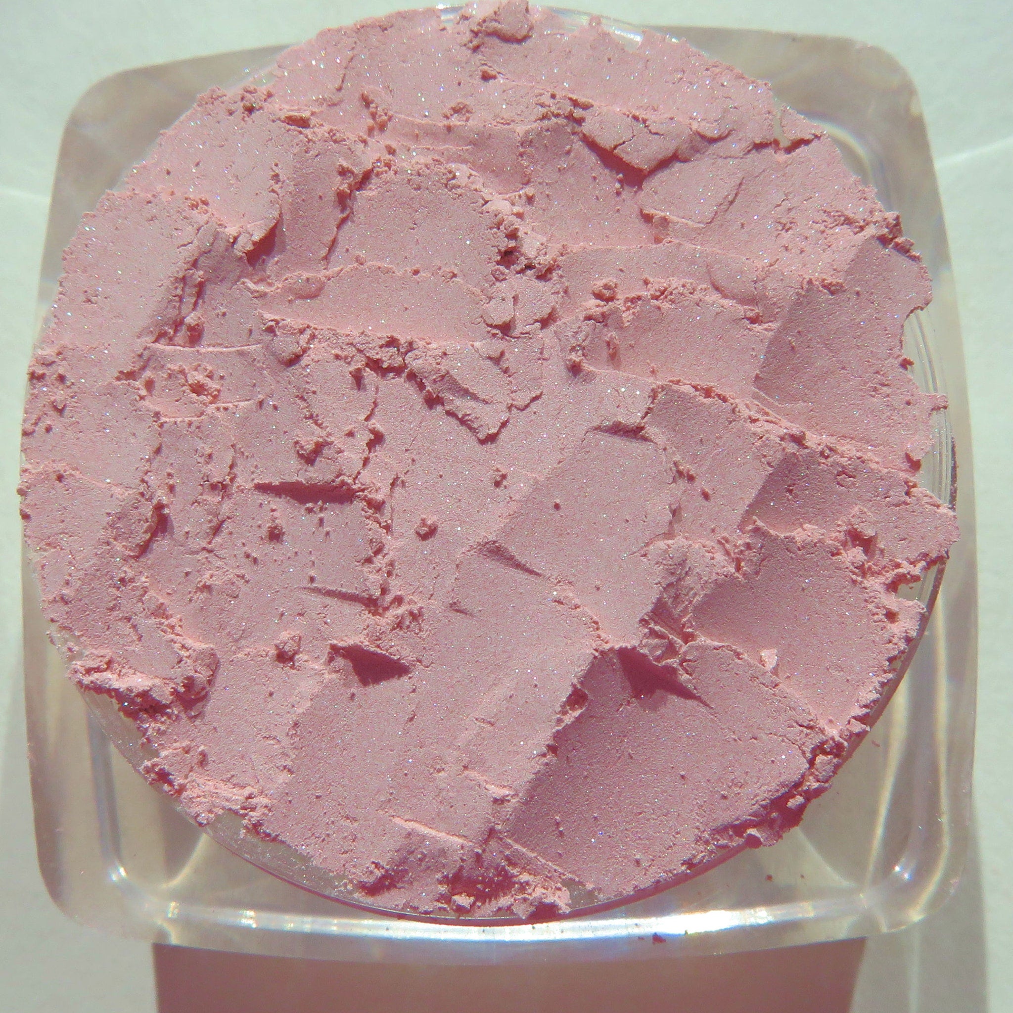 Pastel pink loose powder eyeshadow in a clear glass jar with black screw-top lid and seashell-shaped sifter.