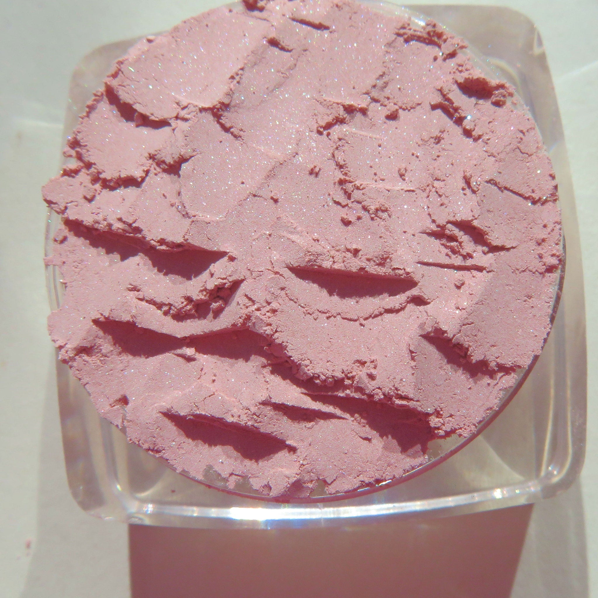 Close-up of pastel pink loose powder eyeshadow with fine shimmer in a seashell-shaped container