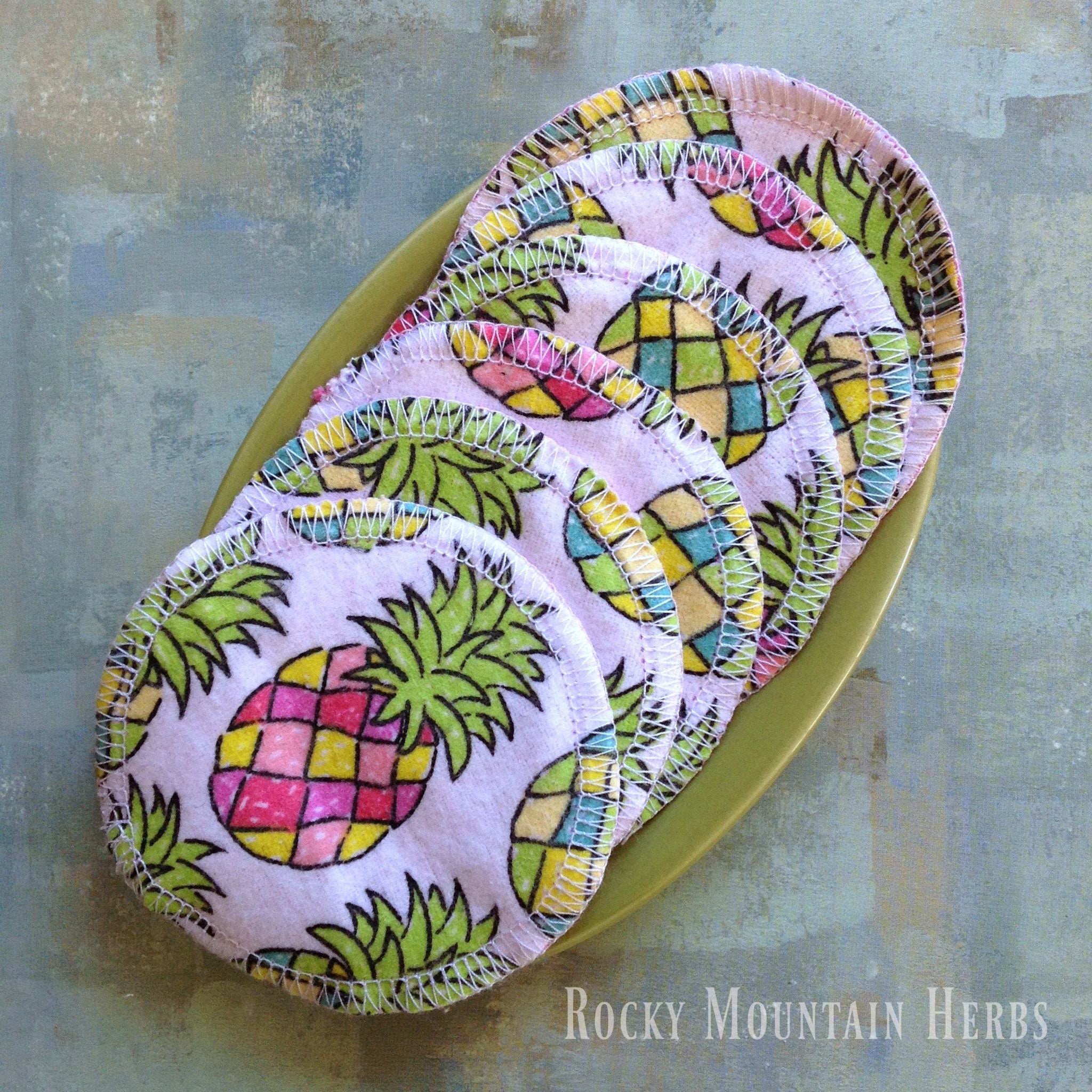 Reusable cotton facial rounds with pineapple print, white stitching, and visible Rocky Mountain Herbs logo