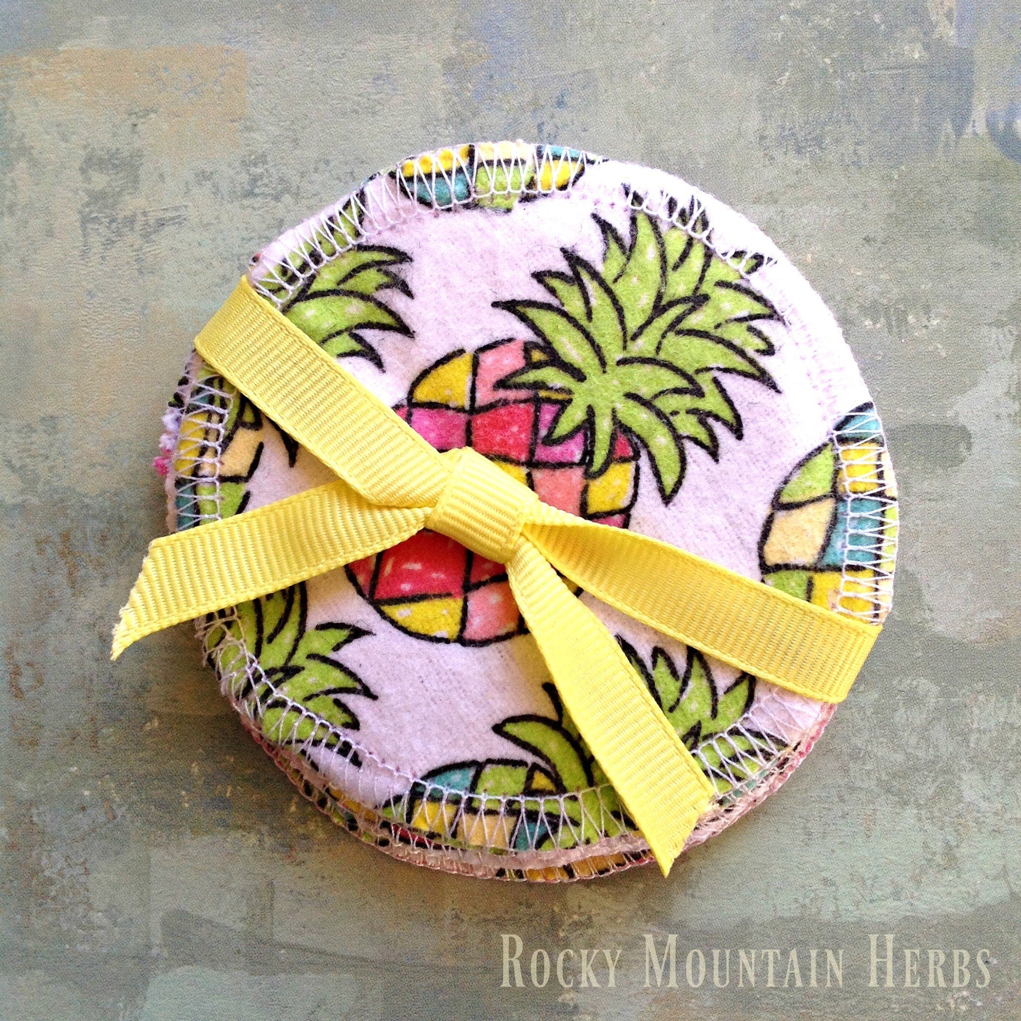 Reusable facial rounds with pineapple pattern, yellow ribbon bow, and white stitched edges