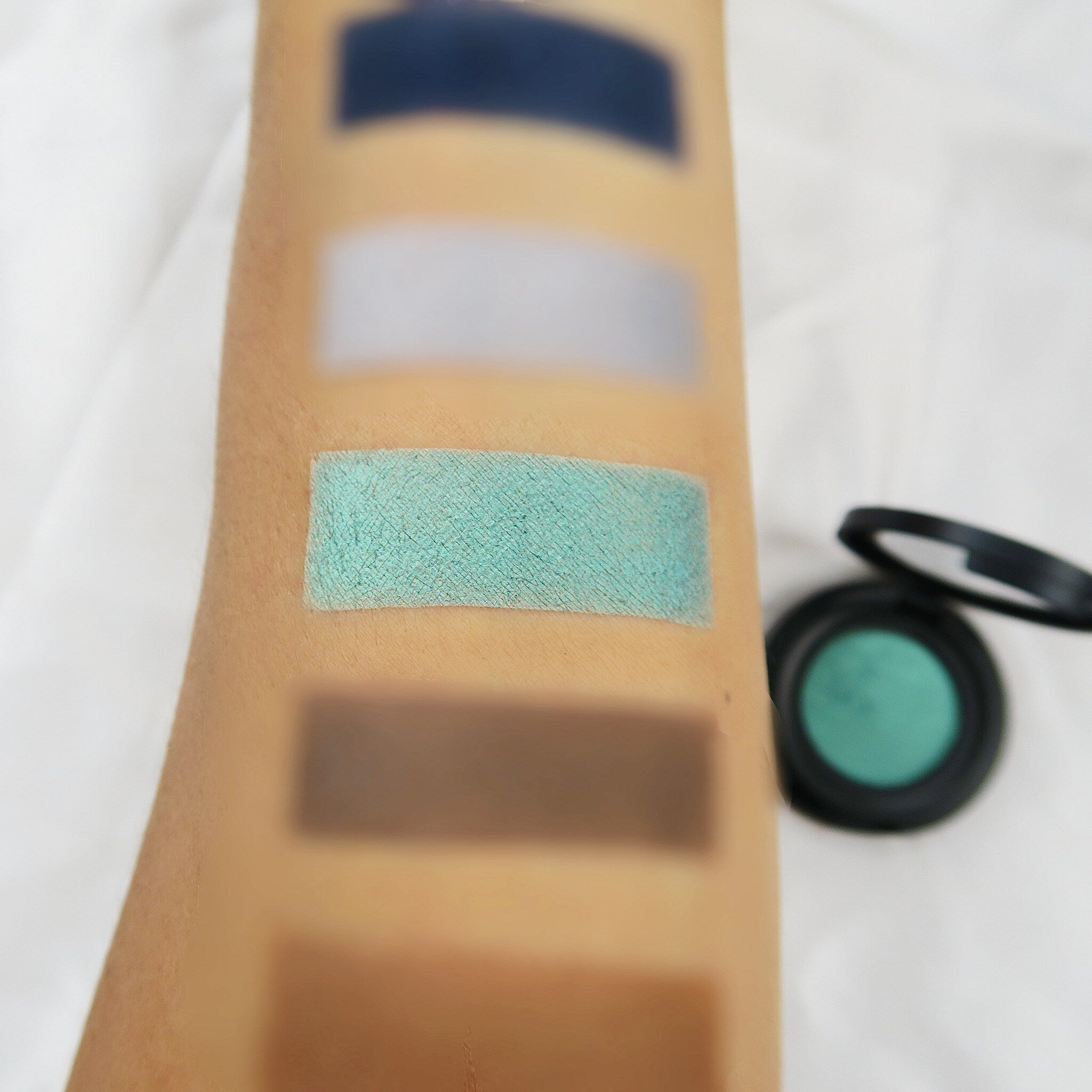 Side view of vegan mermaid green eyeshadow pan showing shimmer finish and compact size