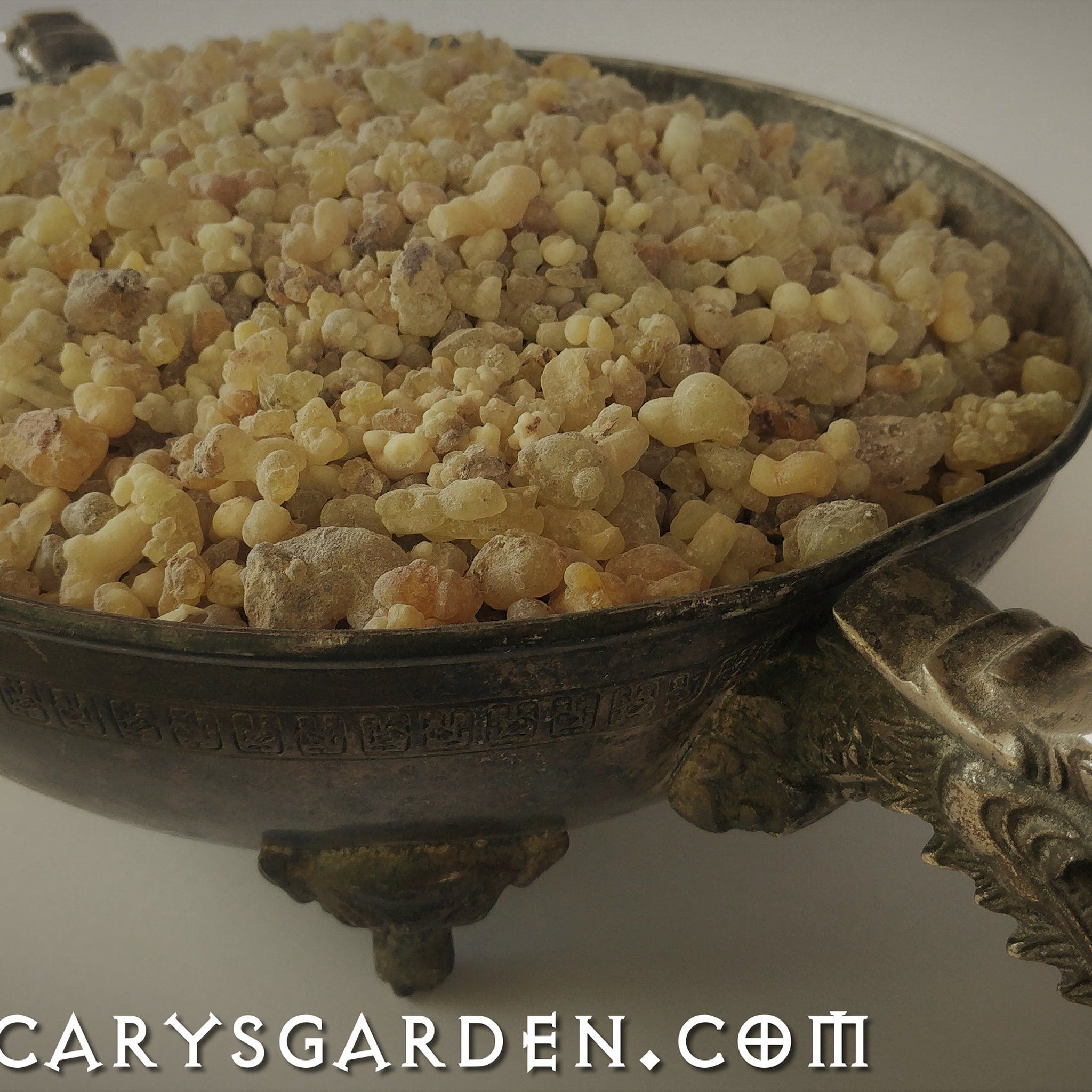 Incense resin granules, light yellow and brown, in a decorative metal bowl, Carysgarden logo visible